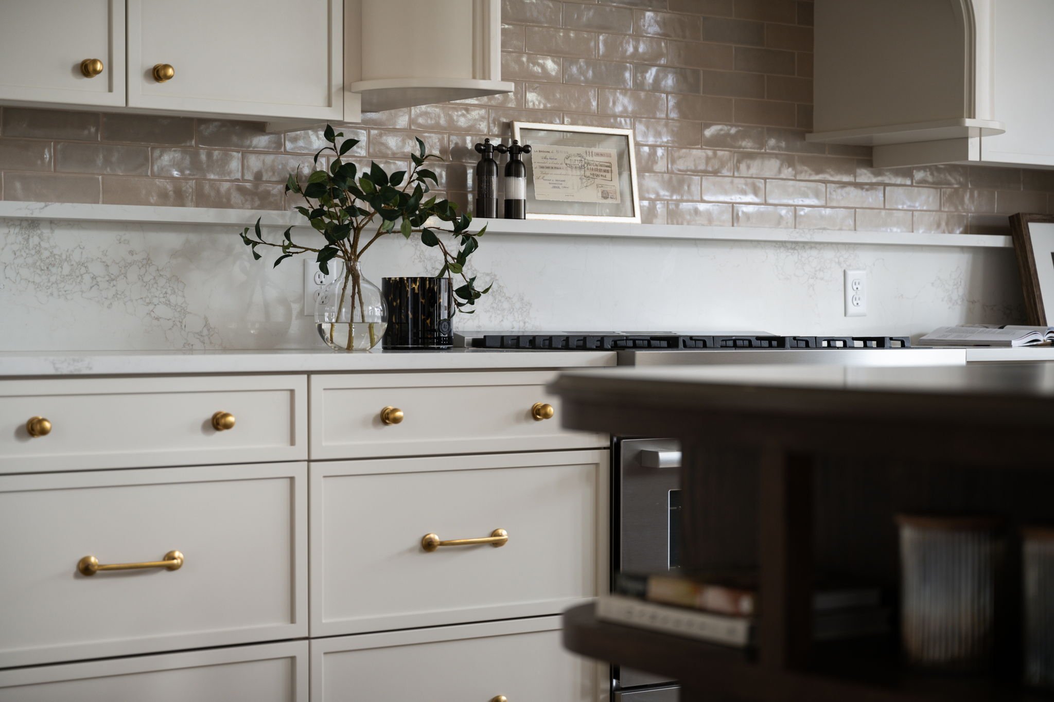 Modern kitchen with white cabinets, gold knobs, black and white accessories, houseplants, and a framed certificate.