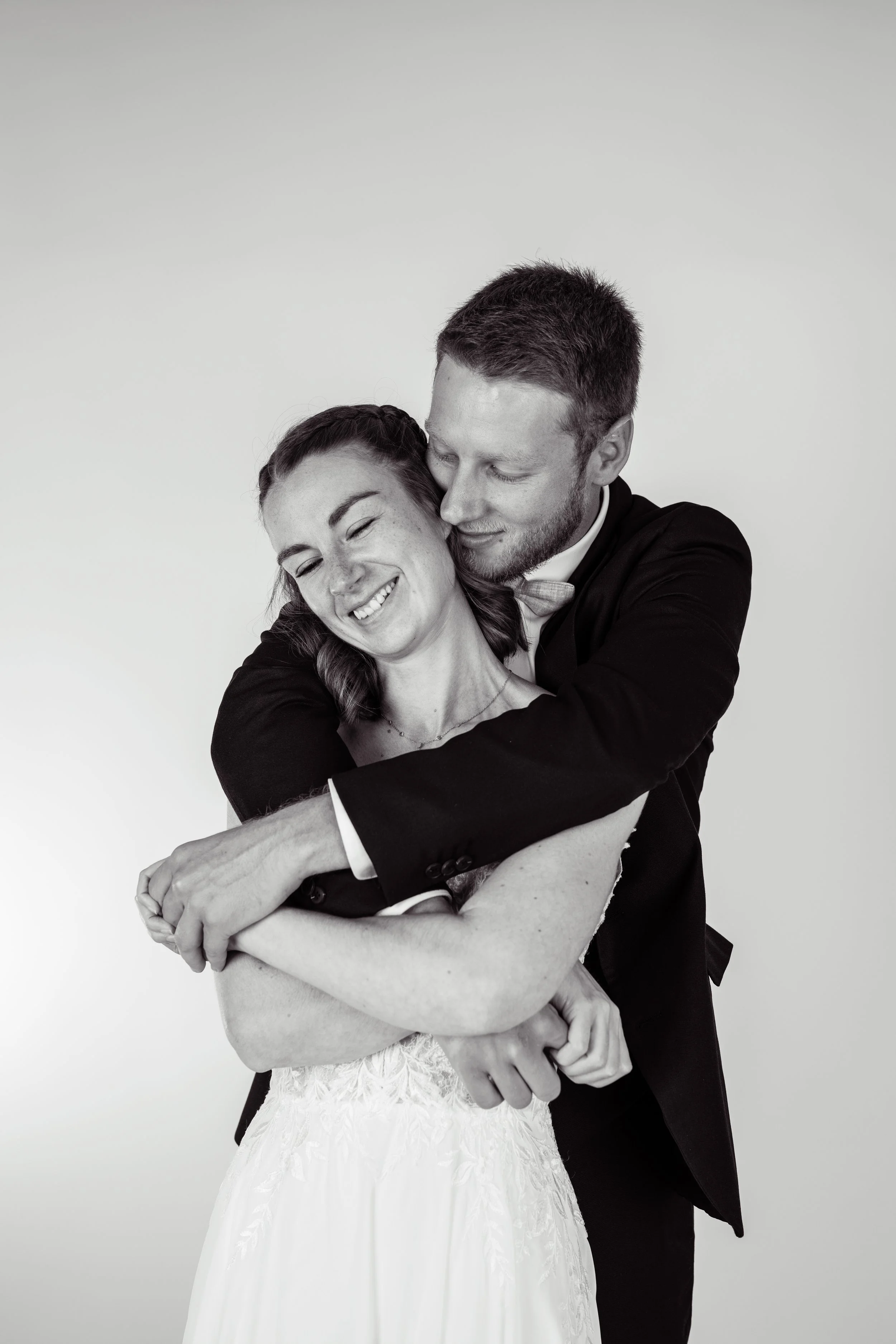 Un couple en habits de mariage s'embrasse et sourit, en noir et blanc.