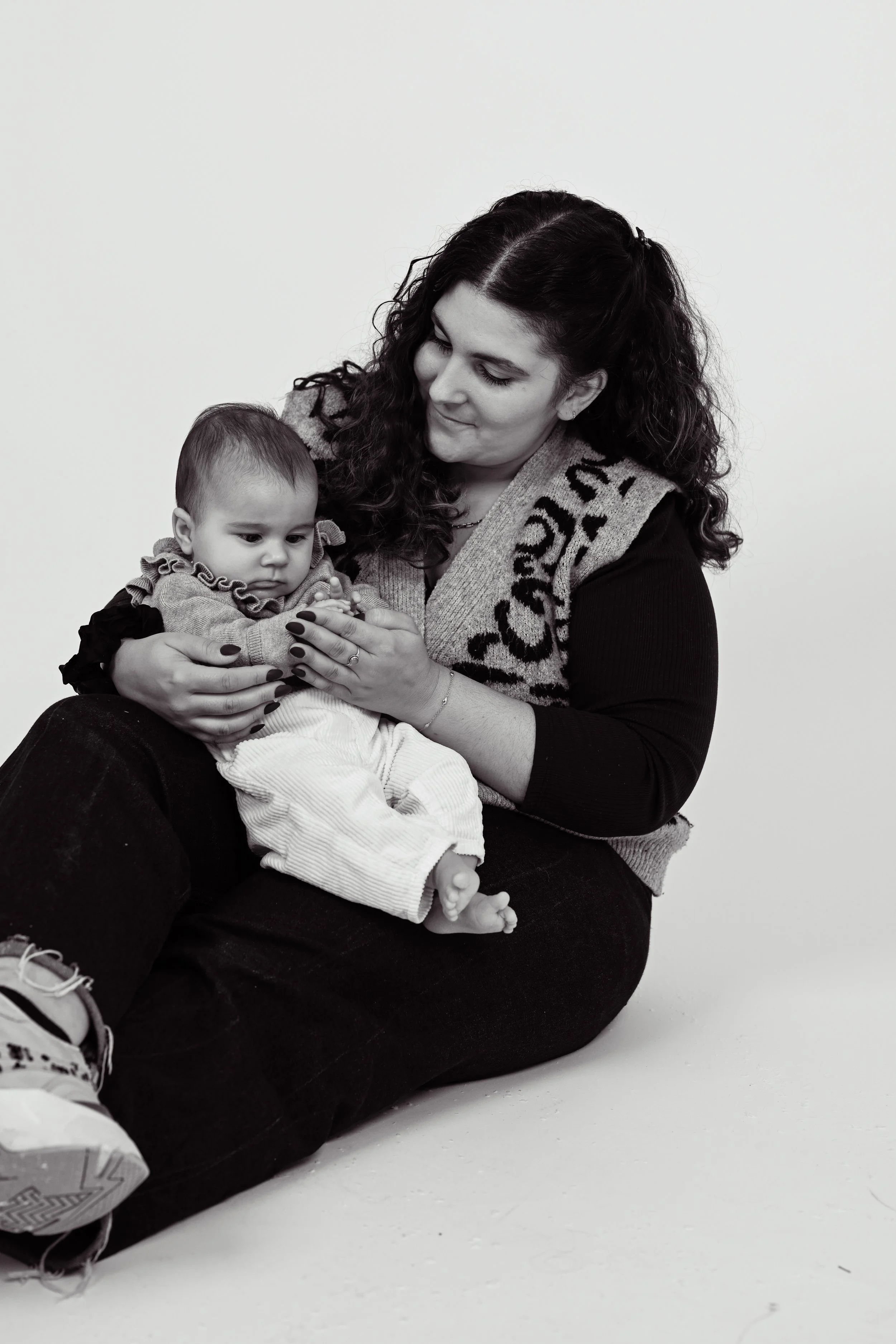 Une femme assise sur le sol tient un bébé dans ses bras. La femme regarde tendrement le bébé. L'image est en noir et blanc.