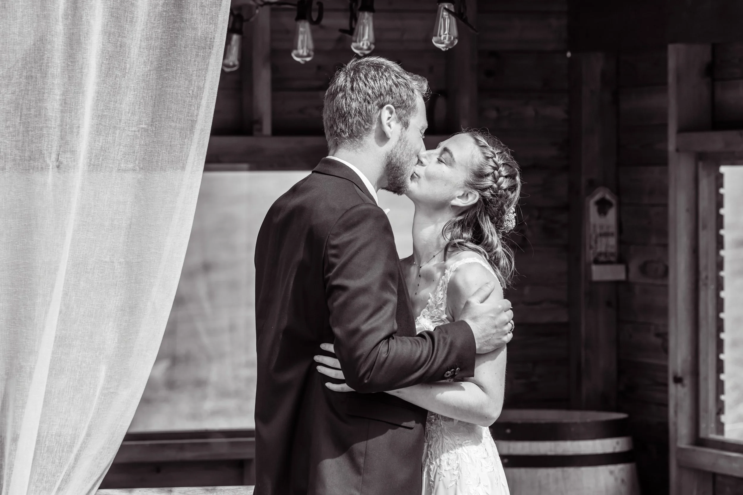 Un couple de mariés s'embrassant lors de leur mariage, dans un cadre rustique en bois.