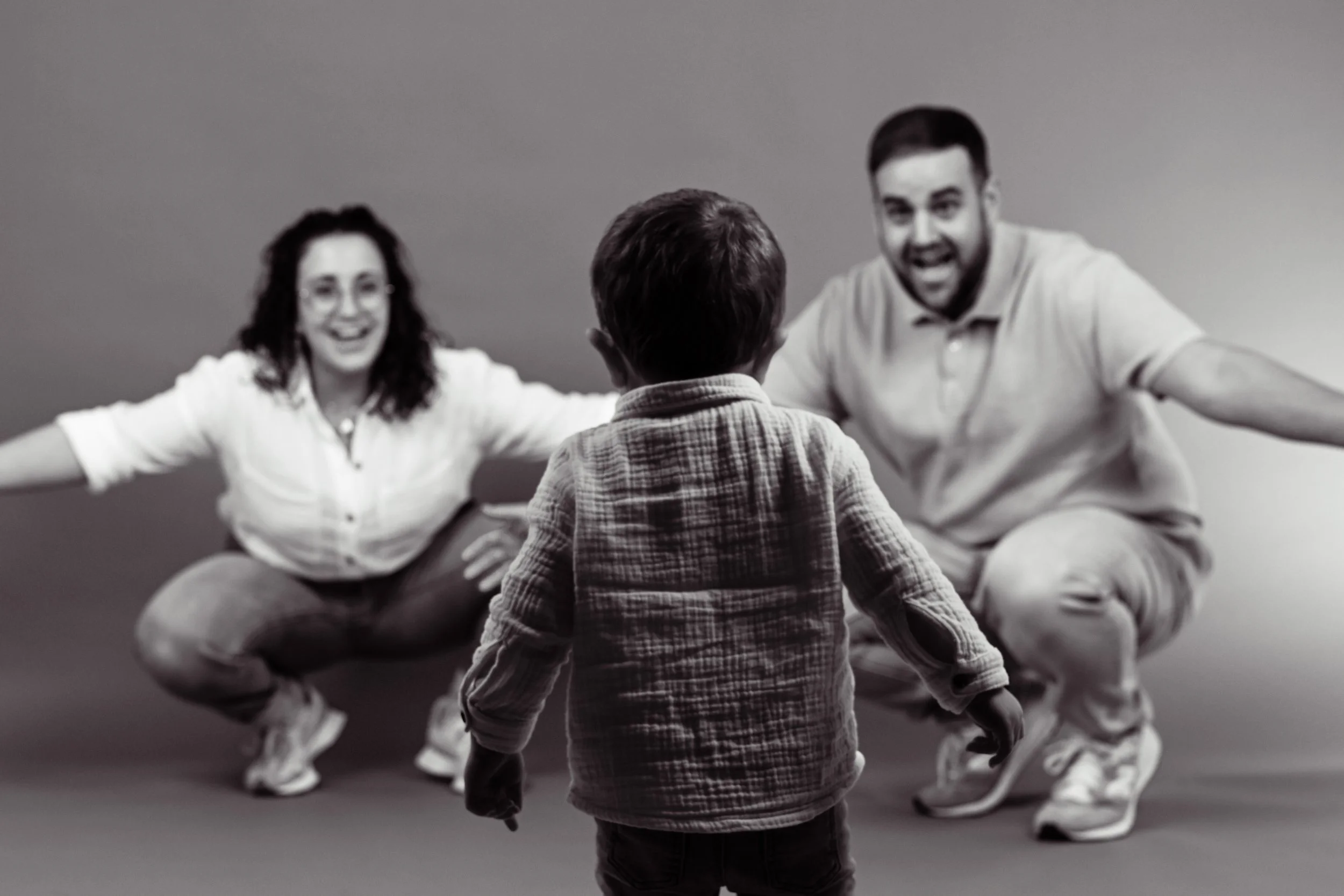 Un enfant regardant un couple d'adultes avec des expressions joyeuses sur fond gris.