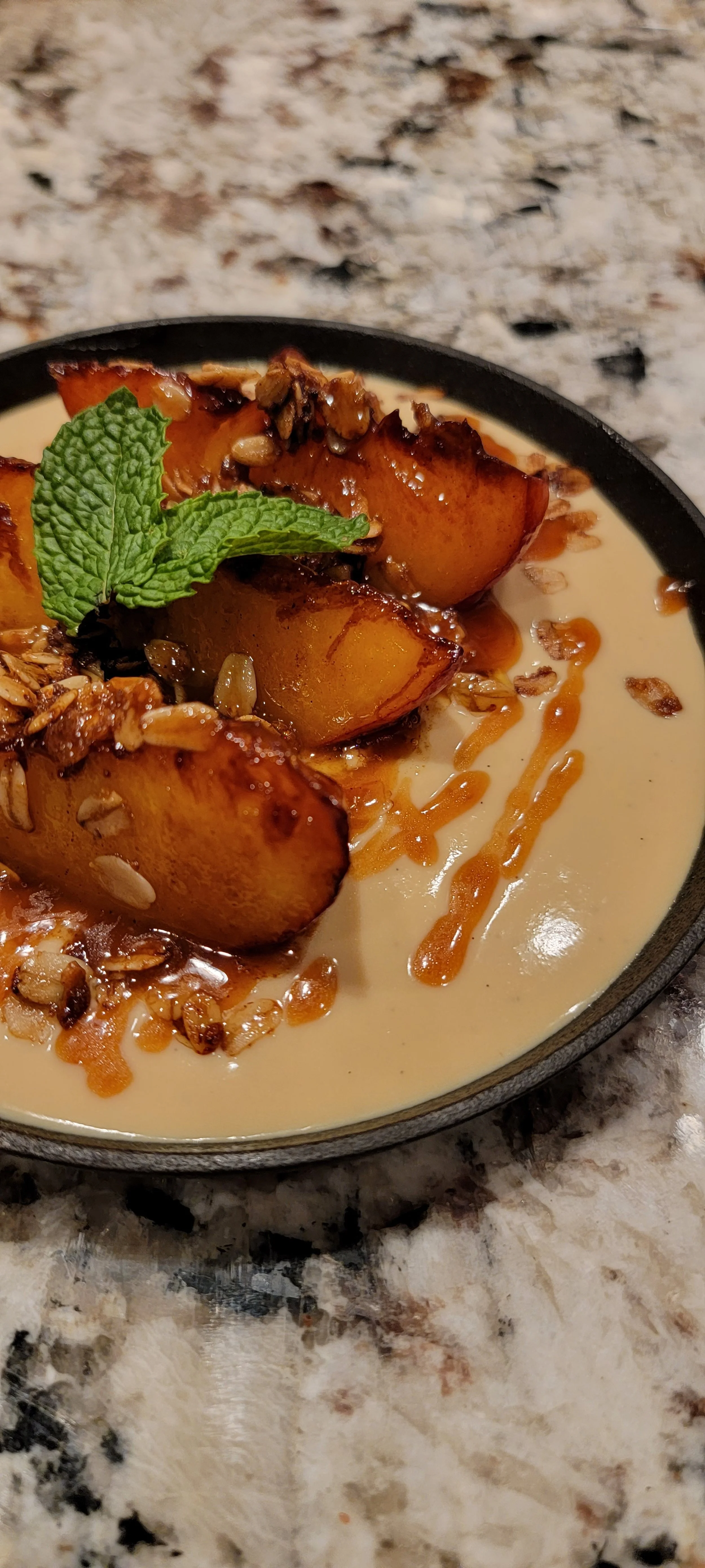 Close-up of roasted peaches garnished with fresh mint, served in a creamy sauce with toasted oats and drizzled caramel sauce.