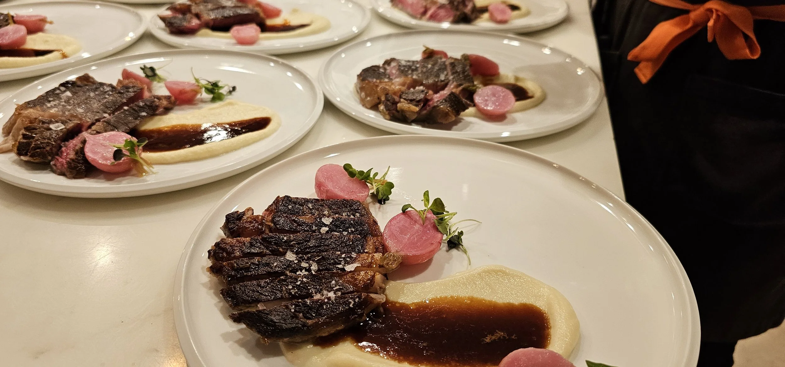 Plates of sliced cooked steak with sauce, pink radish slices, and green microgreens.