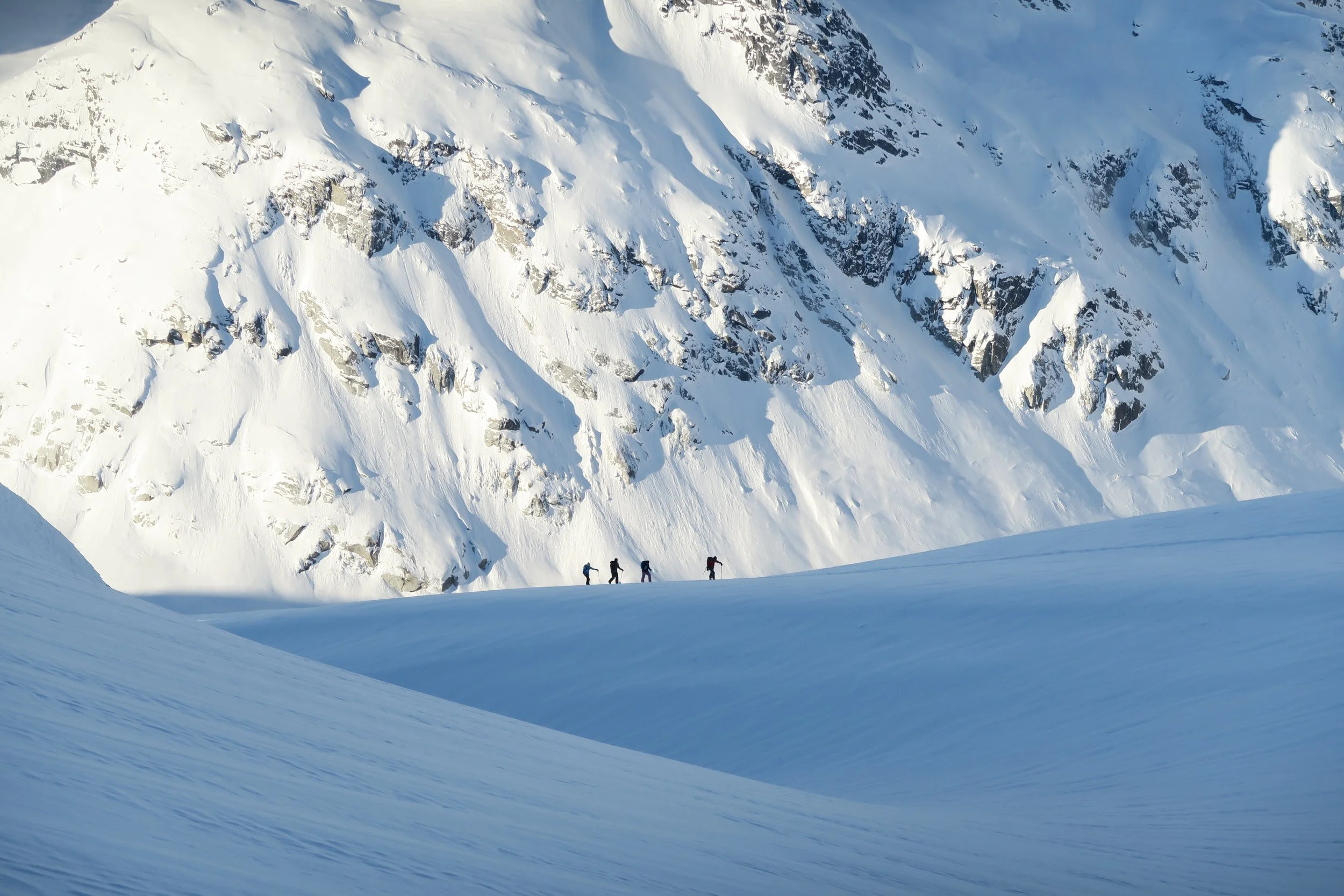 A group of five people hiking in snowy, mountainous terrain.
