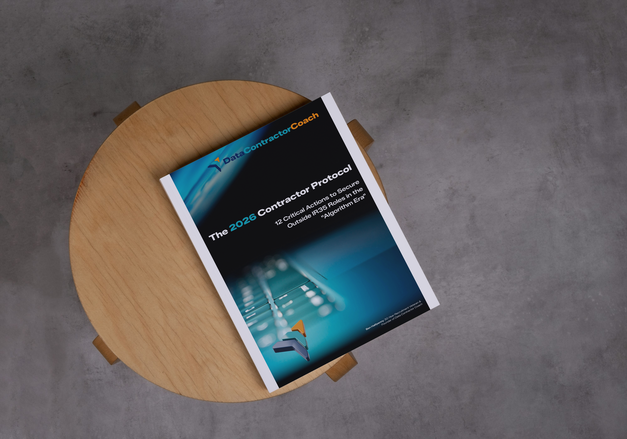 Top view of a paperback book titled 'The 2026 Contractor Protocol' on a round wooden table with a concrete floor background.