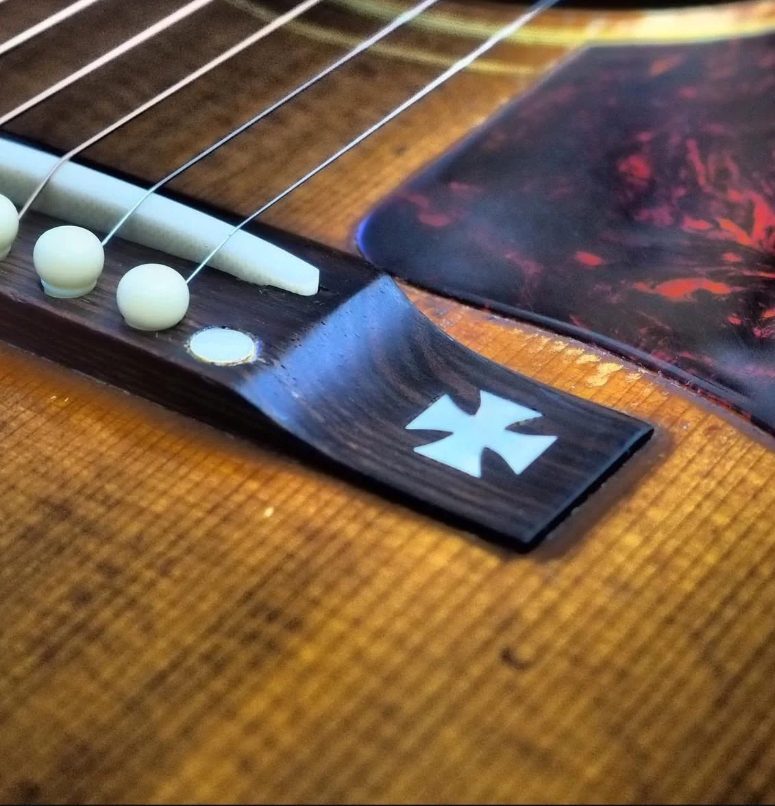 Close-up of an acoustic guitar's bridge with white bridge pins, strings, a pickguard, and a logo on the body.