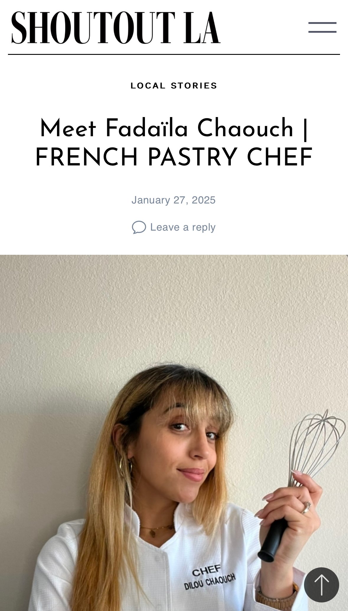 A woman with long blonde hair, wearing a white chef's jacket with 'Chef Dilou Chaouch' embroidered on it, holding a wire whisk and smiling. The background is a plain, beige wall.