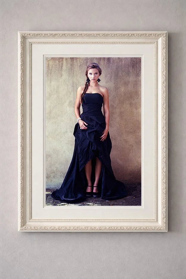 A framed portrait of a woman in a black dress with high heels, standing against a textured background.