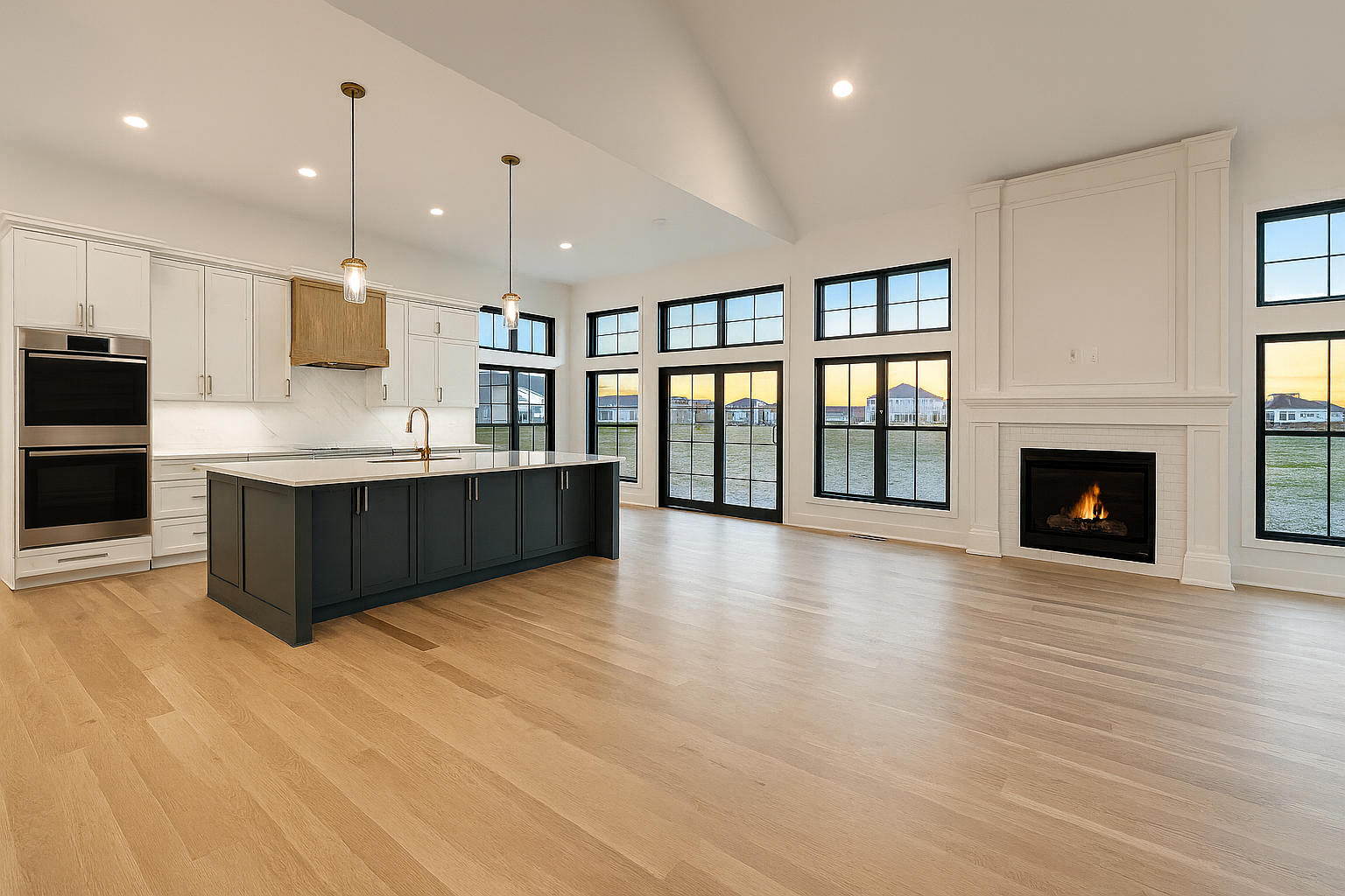 Empty open-concept living room and kitchen with large windows, hardwood floors, a fireplace, and modern white and navy cabinetry.