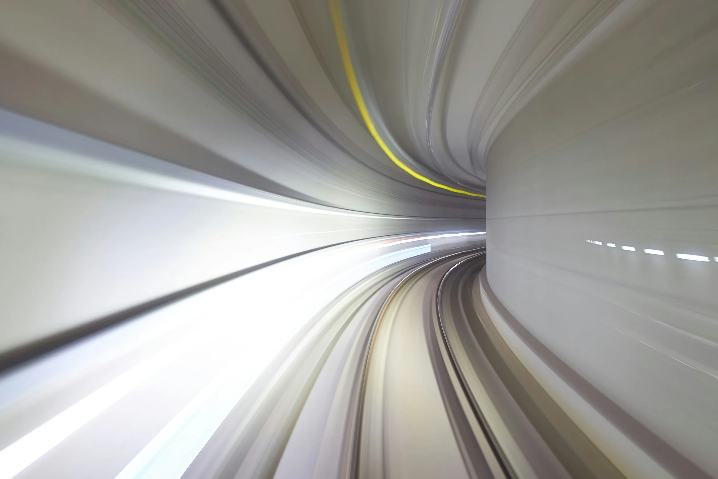 A view inside a tunnel with curved walls and a track, illuminated by white and yellow lights, creating a sense of motion and speed.
