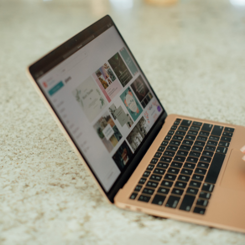 A MacBook laptop on a speckled countertop displaying a website or app with image thumbnails.