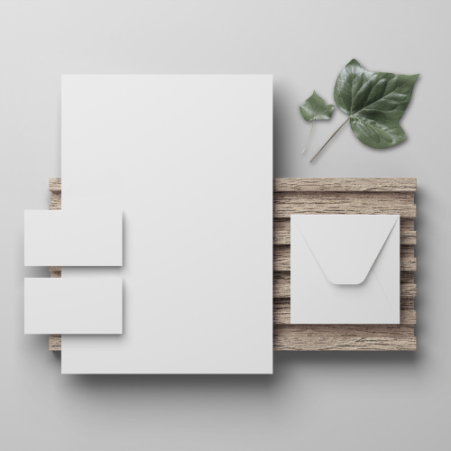 Flat lay of white stationery, an envelope, and green leaves on a wooden board background.