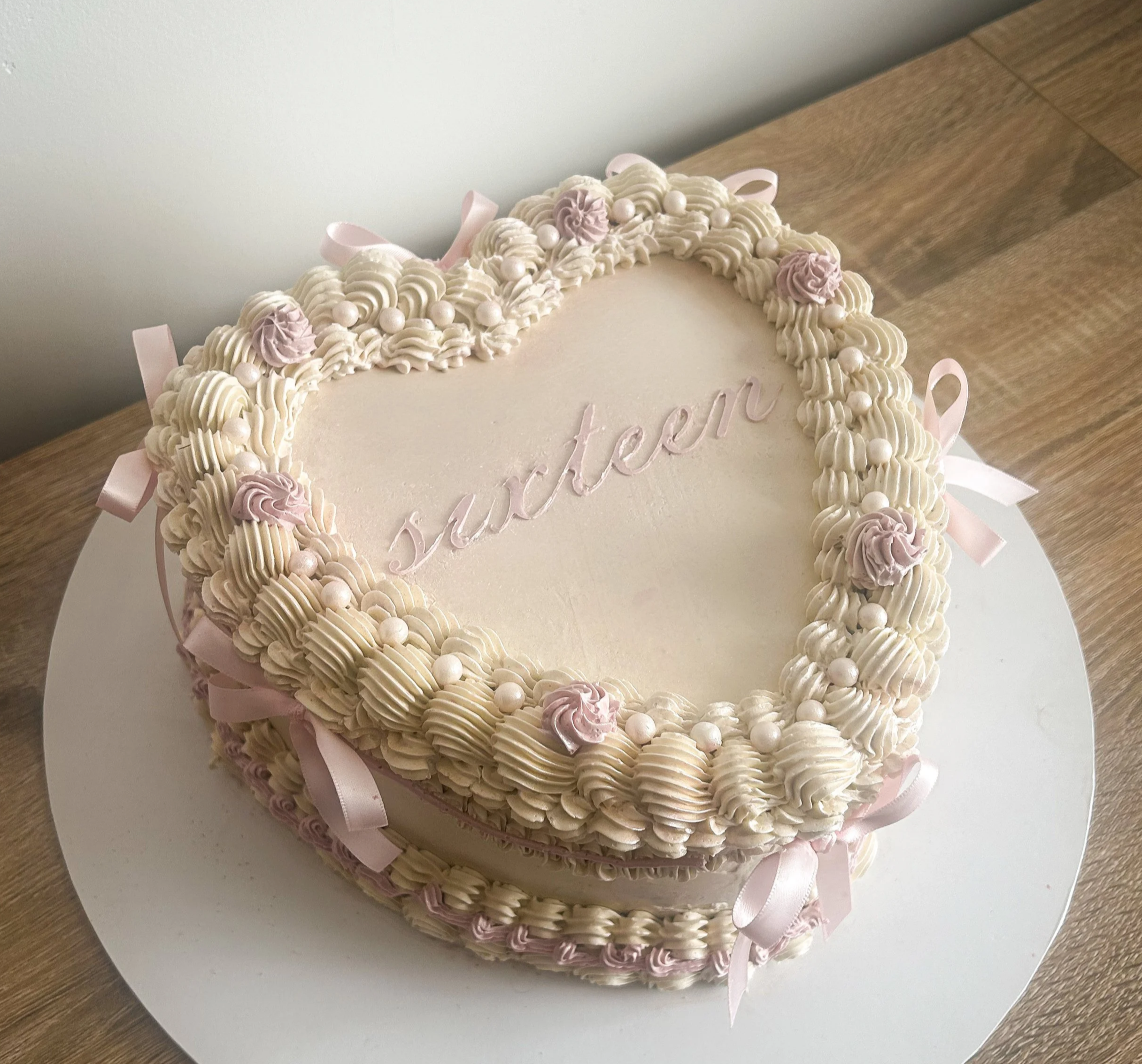 Decorative heart-shaped cake with white and pink frosting, pink ribbons, and the word 'Juster' written on top.