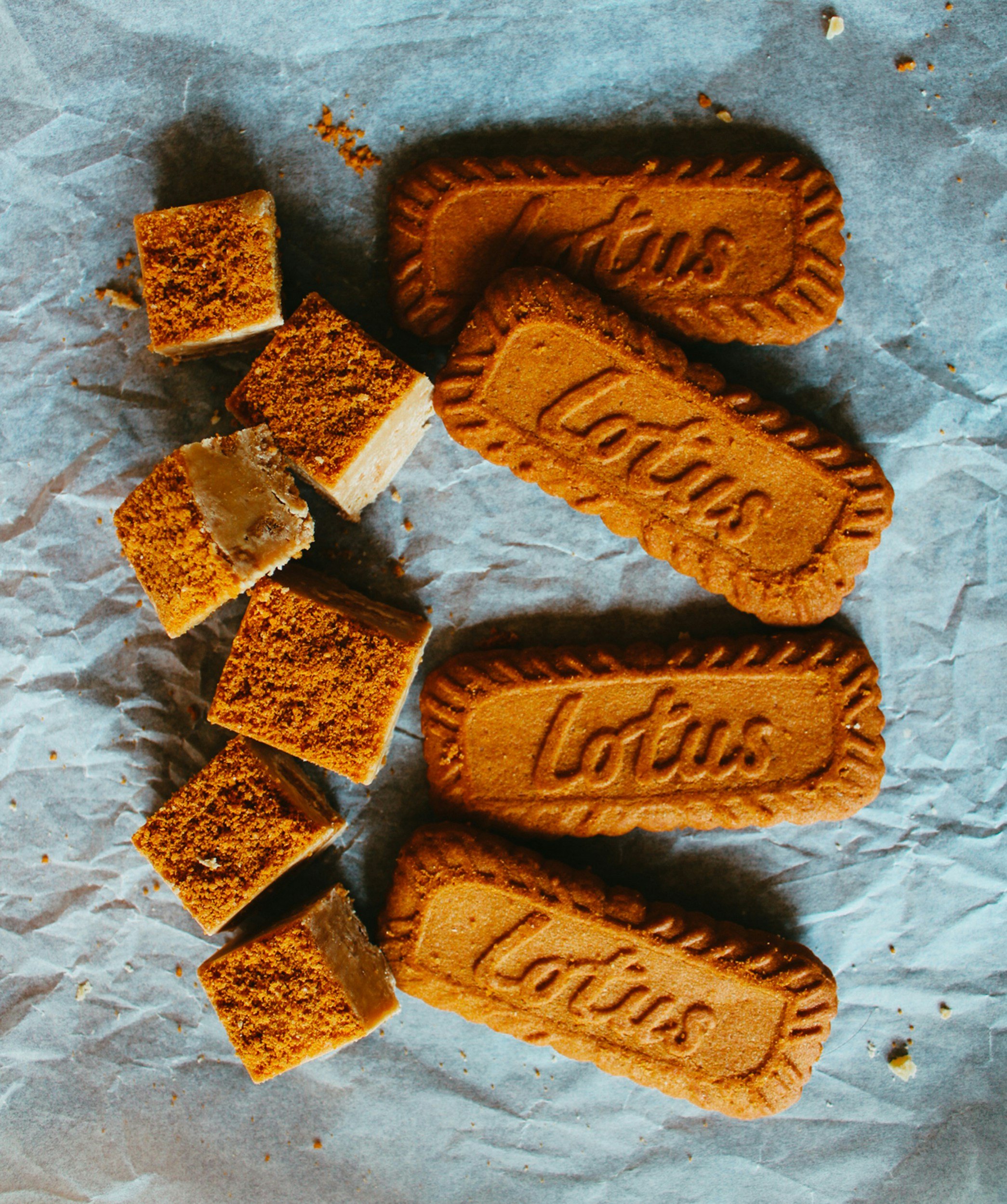 Several Lotus Biscoff cookies, some whole and some broken into pieces, on crumpled wax paper.