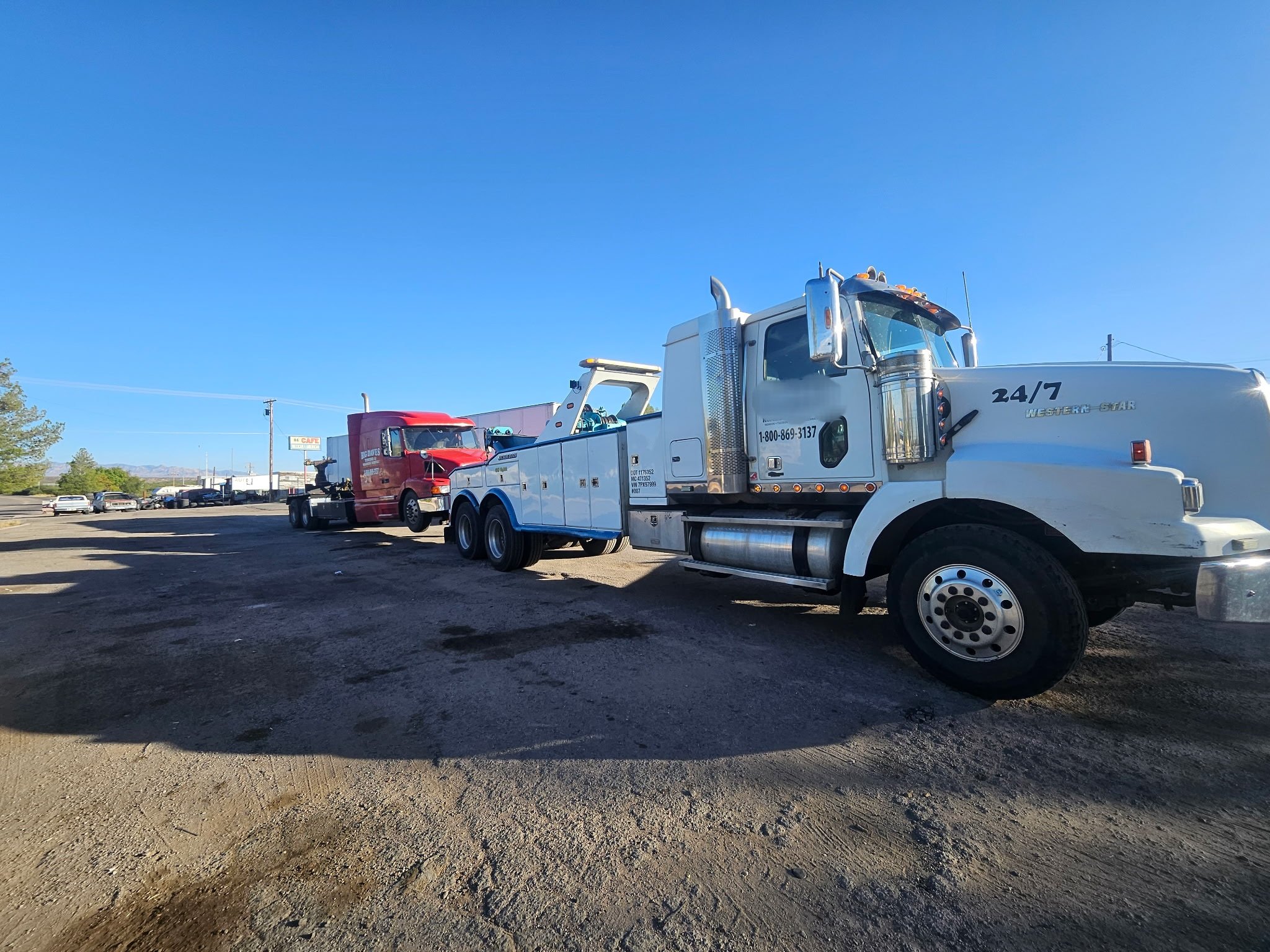 Line of tow trucks parked on a dirt lot with a clear blue sky.