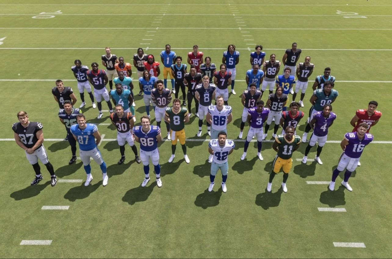 A group of American football players standing on a field, wearing colorful uniforms and helmets, arranged in several rows for a team photo.