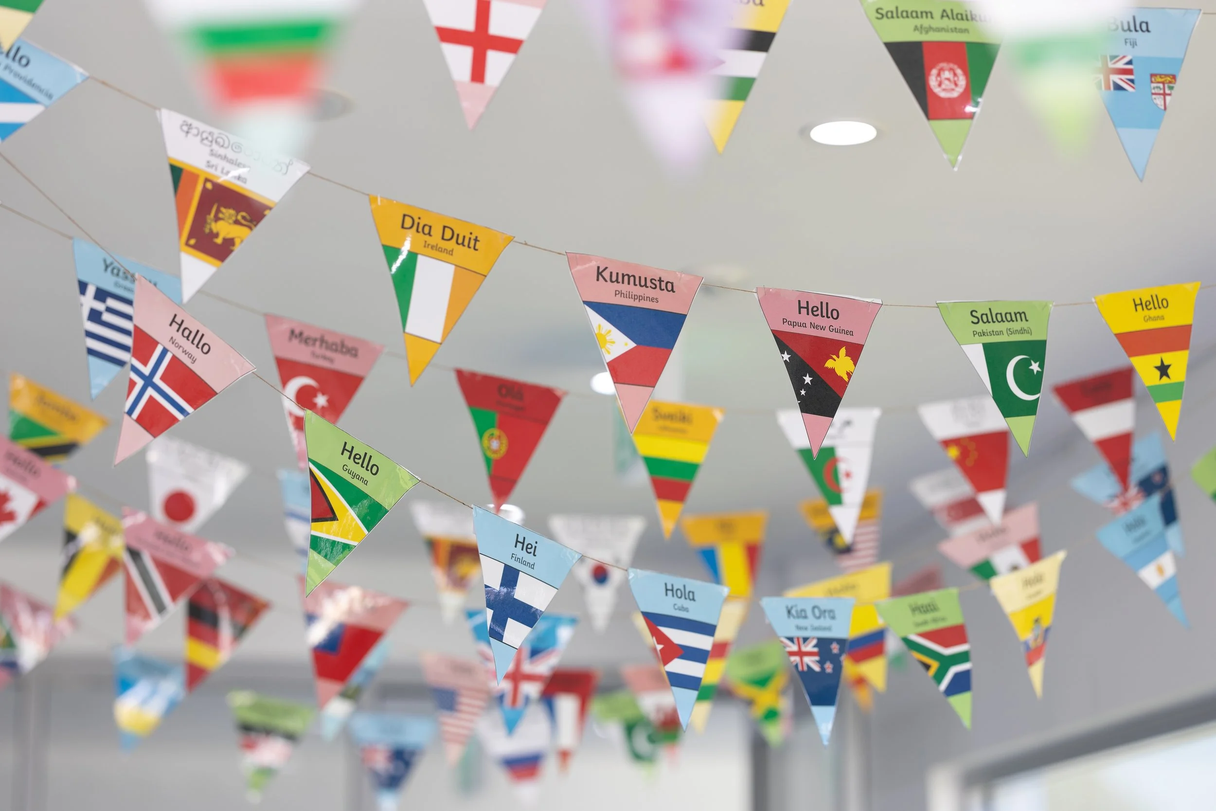 Colorful triangular flags with various country names and flags hanging from a ceiling, representing different nations around the world.