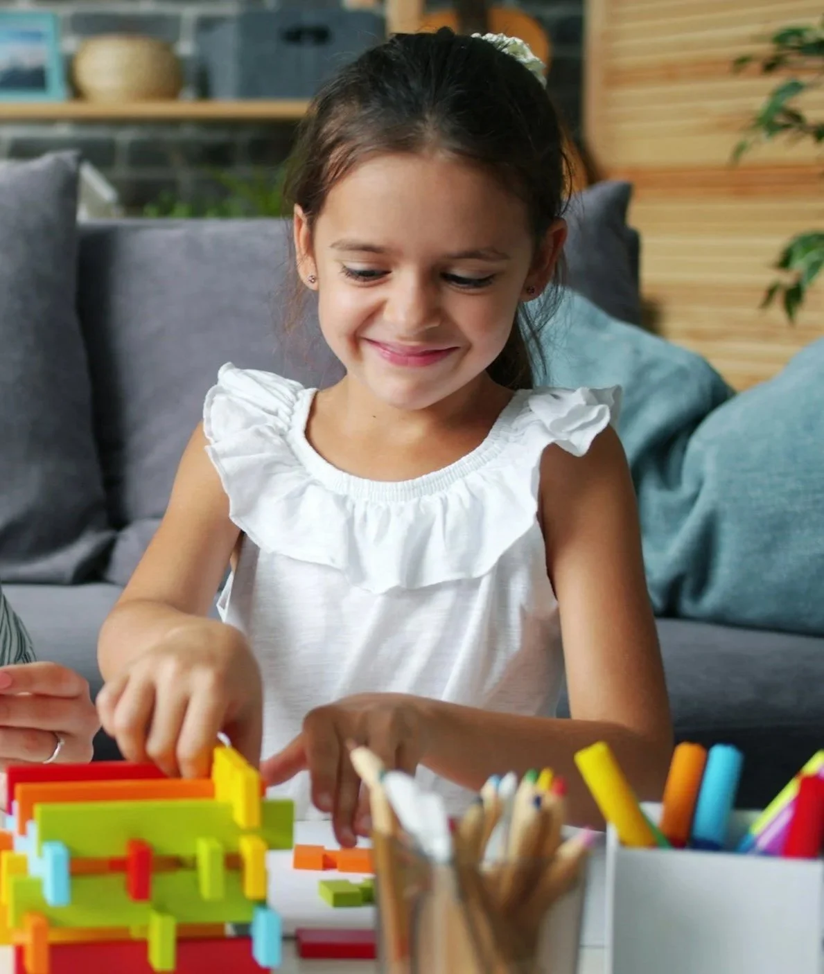 A young girl smiling while playing a colorful plastic maze game on the table in a cozy living room.