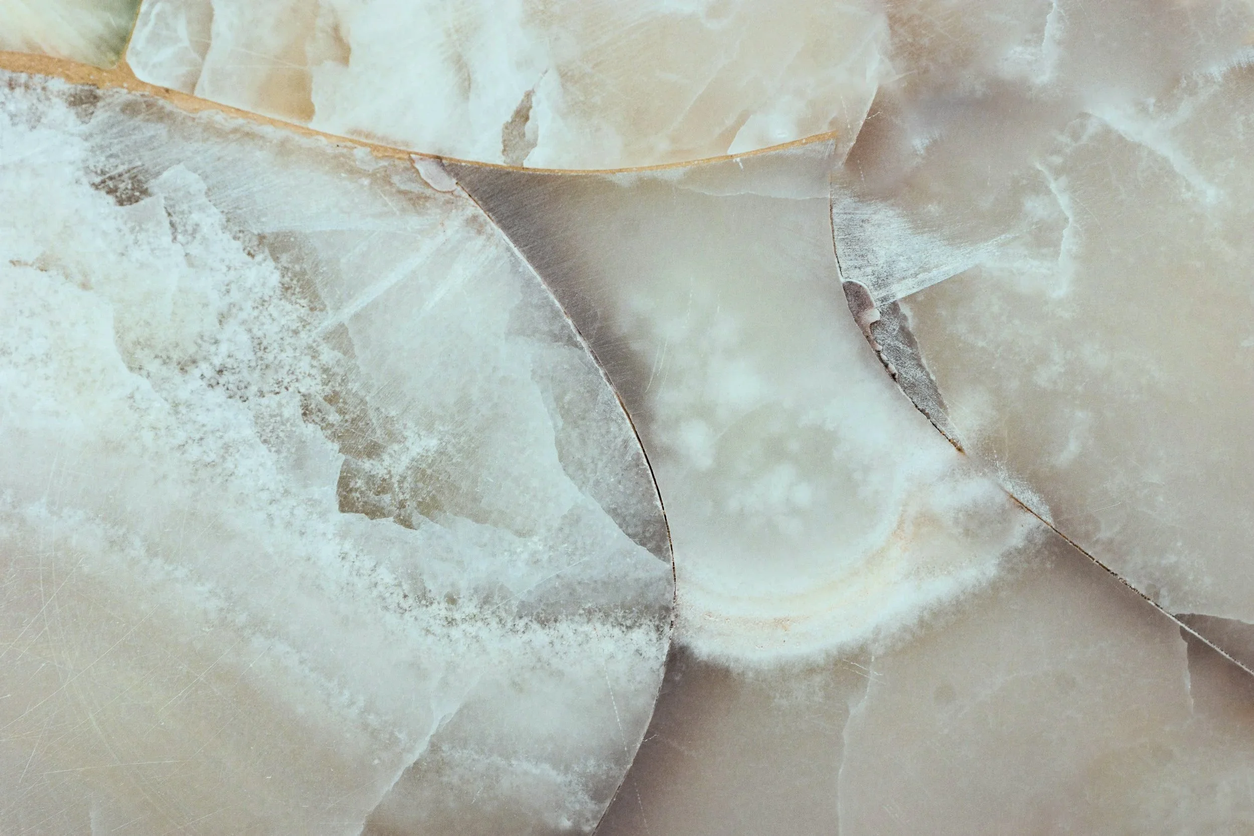 Close-up of layered, translucent mineral or stone with earthy beige, gray, and white tones, showing textured and veined surfaces.
