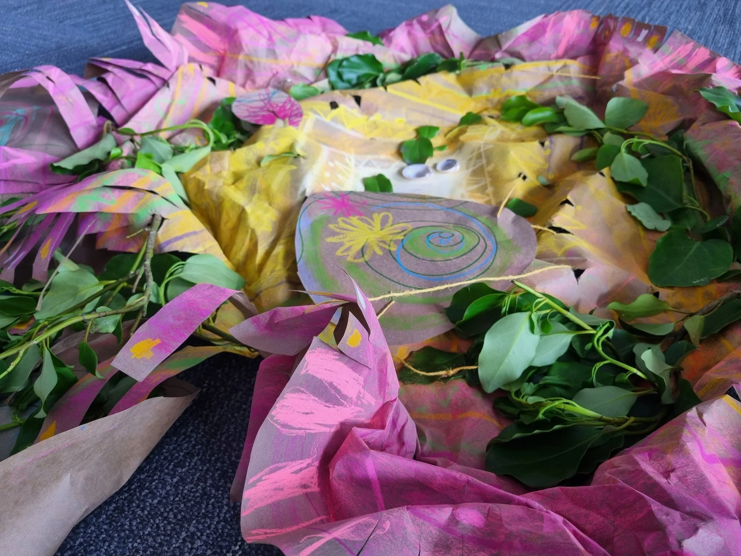 An art project or craft featuring paper, leaves, and drawings on paper, arranged on a dark carpeted surface.