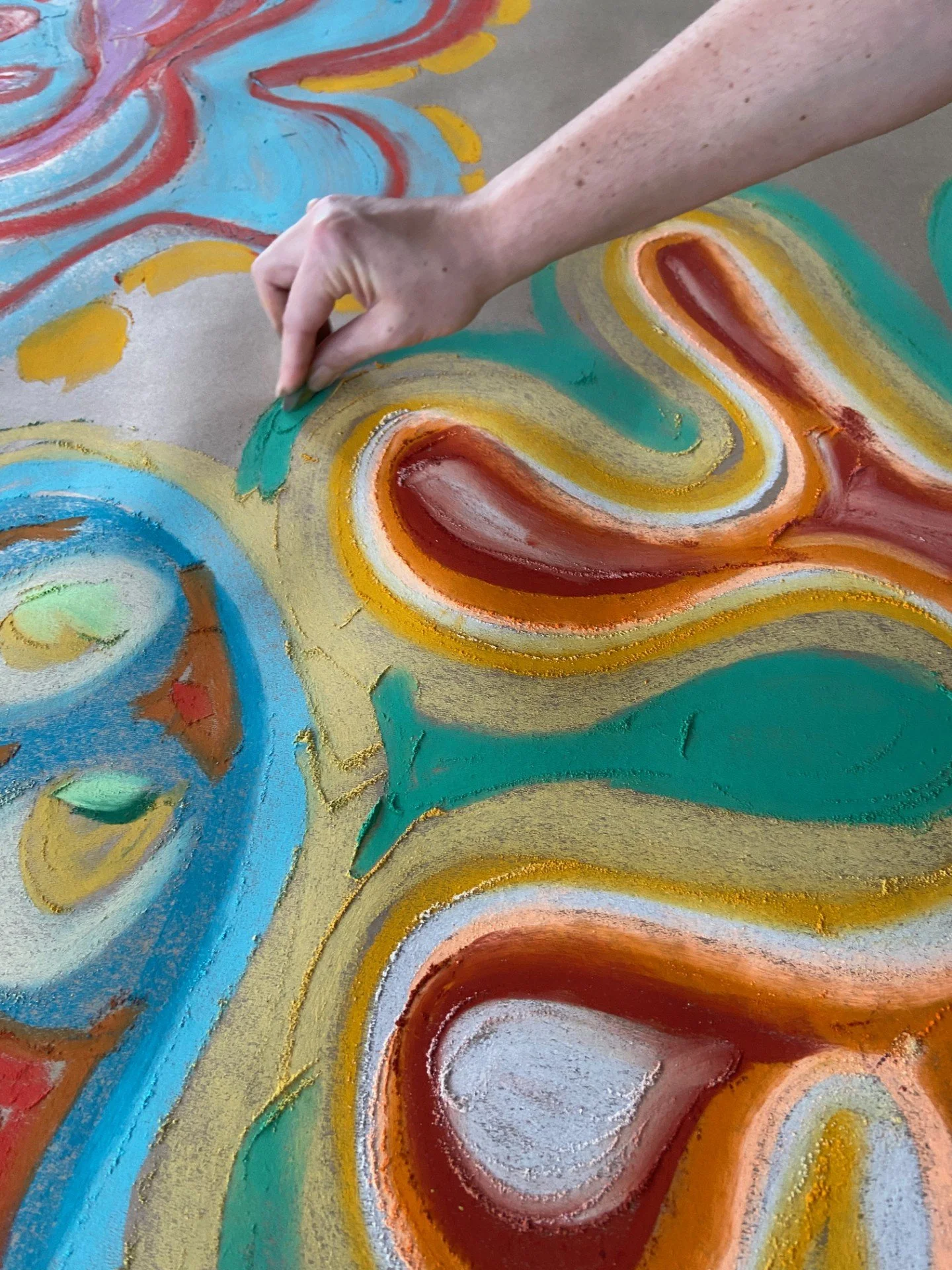 Close-up of a hand painting a colorful, abstract mural with swirls, hearts, and floral designs in bright colors like blue, red, yellow, green, and white.