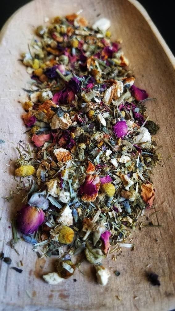 Dried herbal flower mixture with pink, yellow, and white petals and green leaves on a wooden surface.
