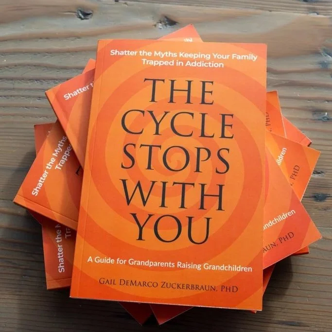 Stack of orange books titled 'The Cycle Stops with You' by Gail DeMarco Zuckerberg, PhD, about breaking family myths and raising grandchildren.
