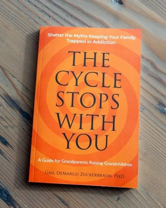 A book titled "The Cycle Stops with You" on a wooden surface. The subtitle reads "A Guide for Grandparents Raising Grandchildren" and the author is Gail DeMarco Zuckerbraun, PhD. The cover has an orange background with circular design elements.