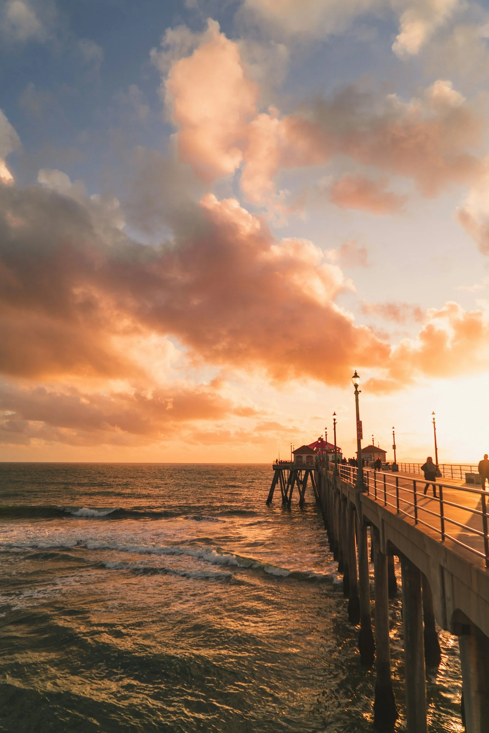 Sunset view at a pier with clouds in the sky and people walking along the boardwalk.