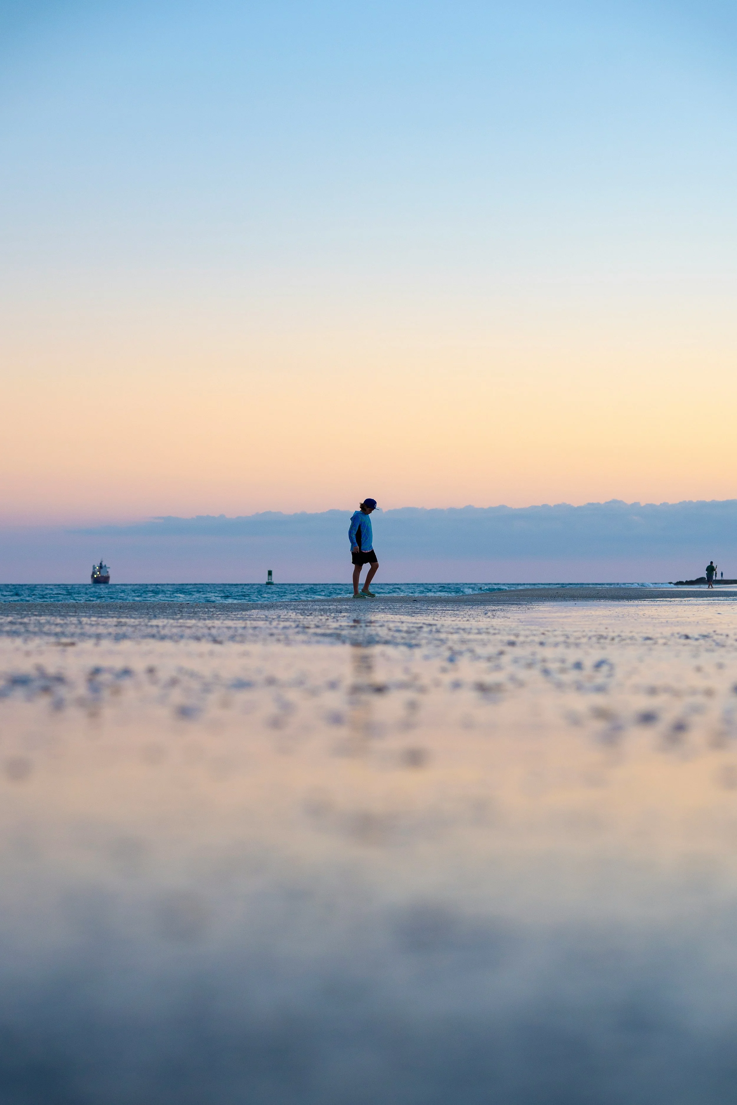 A person walking on a beach during sunset with a ship and a buoy in the distance