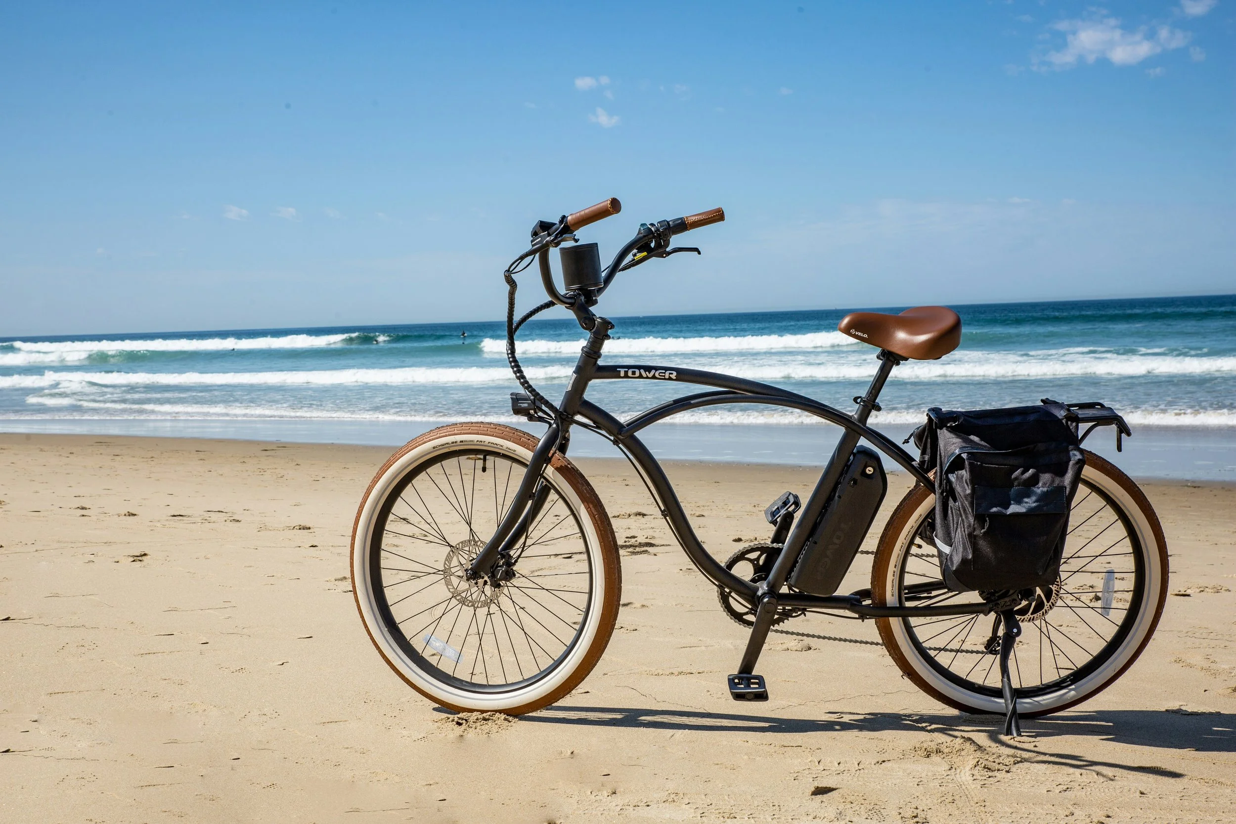 Electric bicycle parked on sandy beach with ocean waves and blue sky in background.