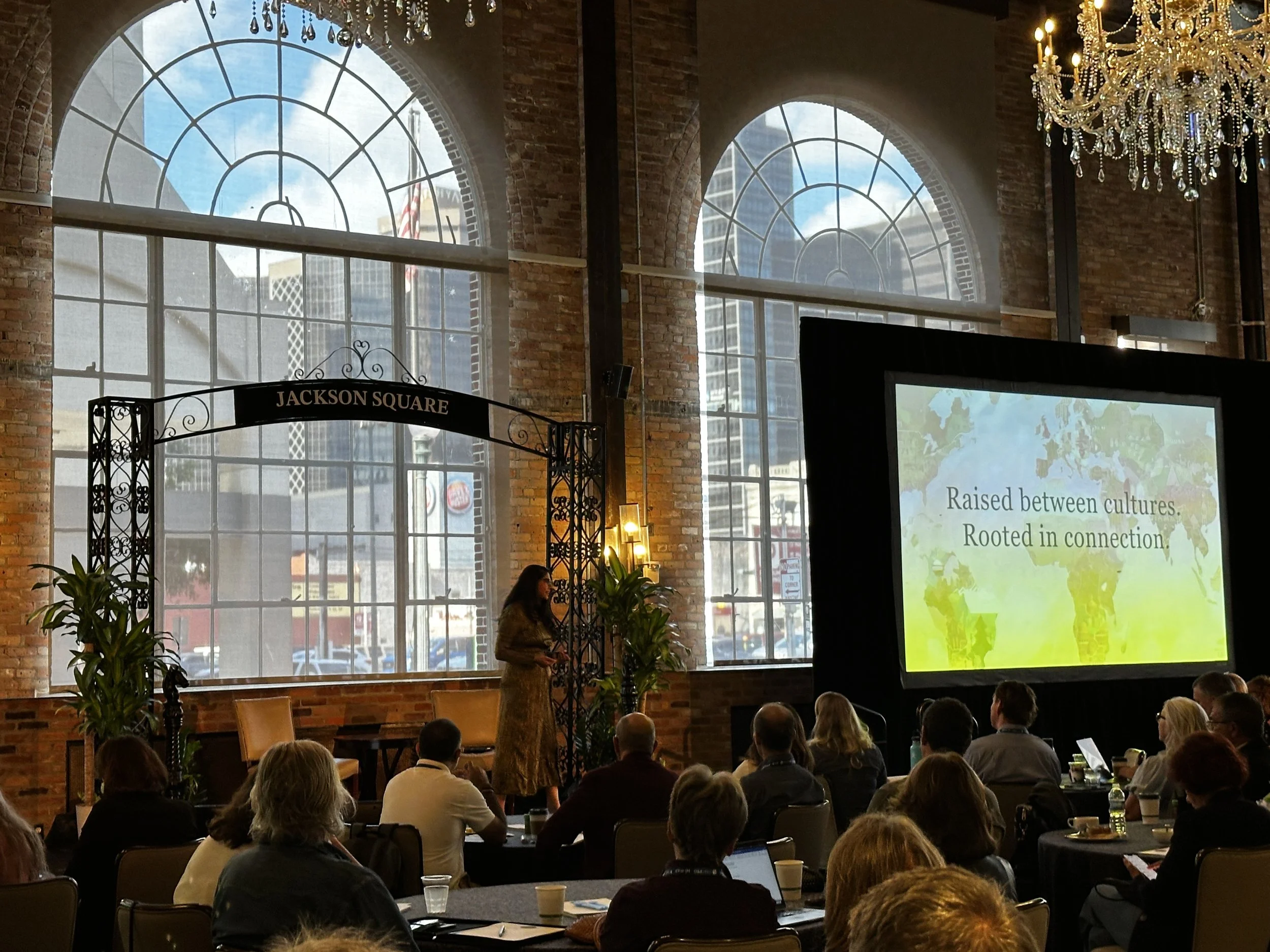 Dr. Payal Beri, PhD speaking in front of a crowd. Large windows are in the background and an arch is over the stage with the words "Jackson Square" at the top.