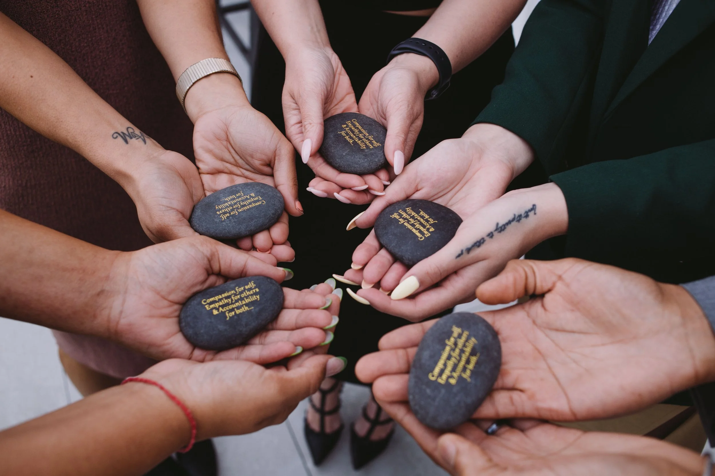 Hands holding stones that read "compassion for self, empathy for others, accountability for both"