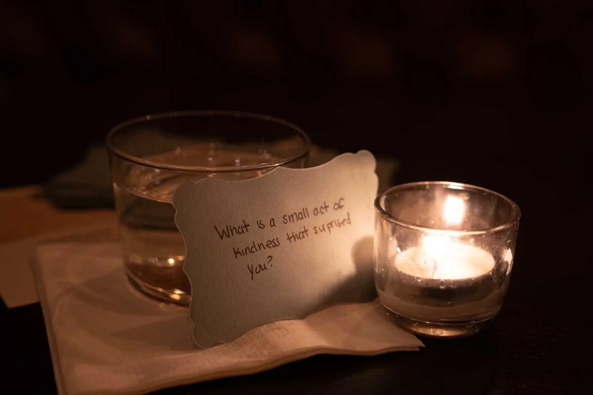 A candle-lit card that says "what is a small act of kindness that surprised you?"