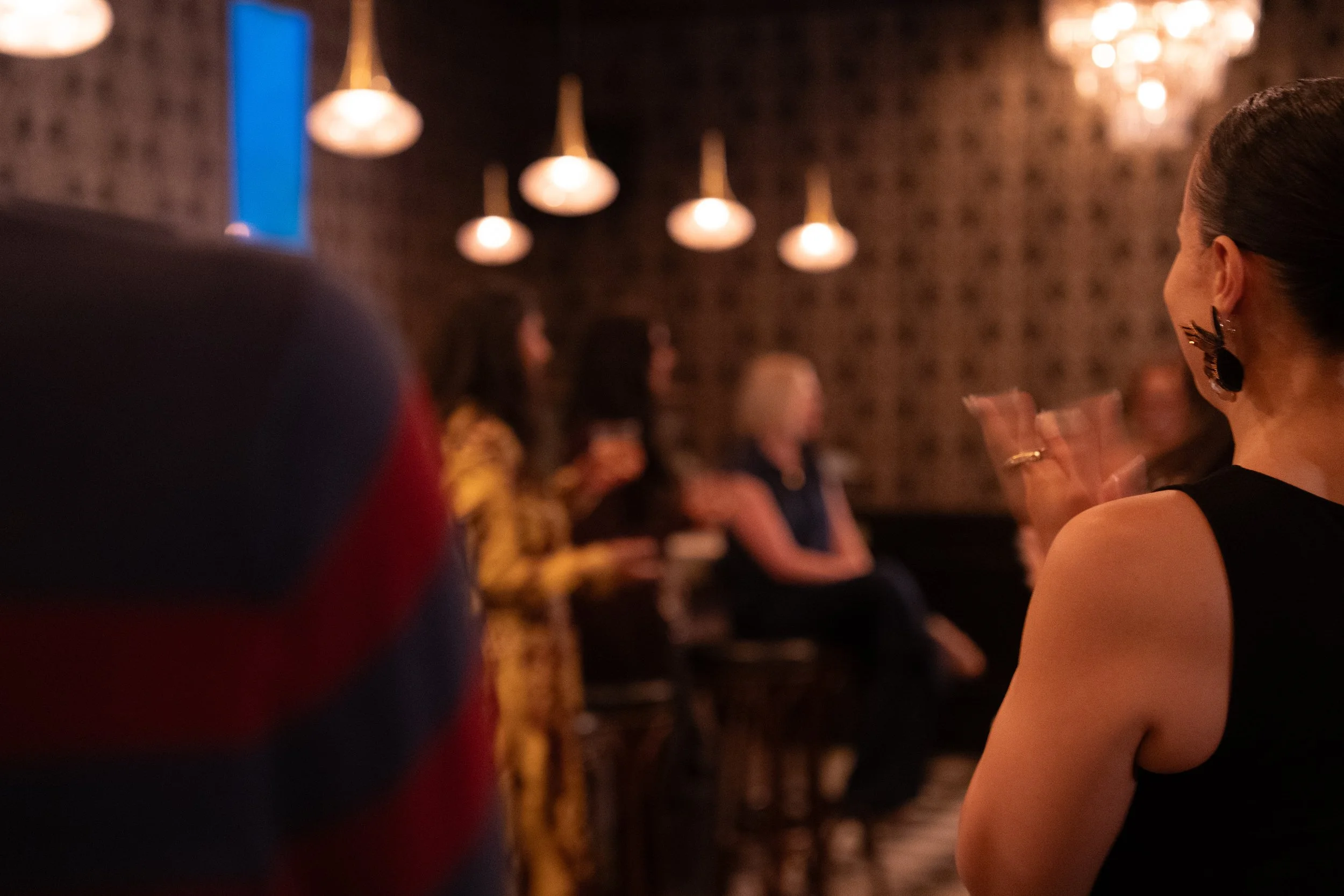 A depth-of-field image of people clapping at a Storyteller's Salon Changemaker's Dinner. They are blurred out, but can be seen clapping.