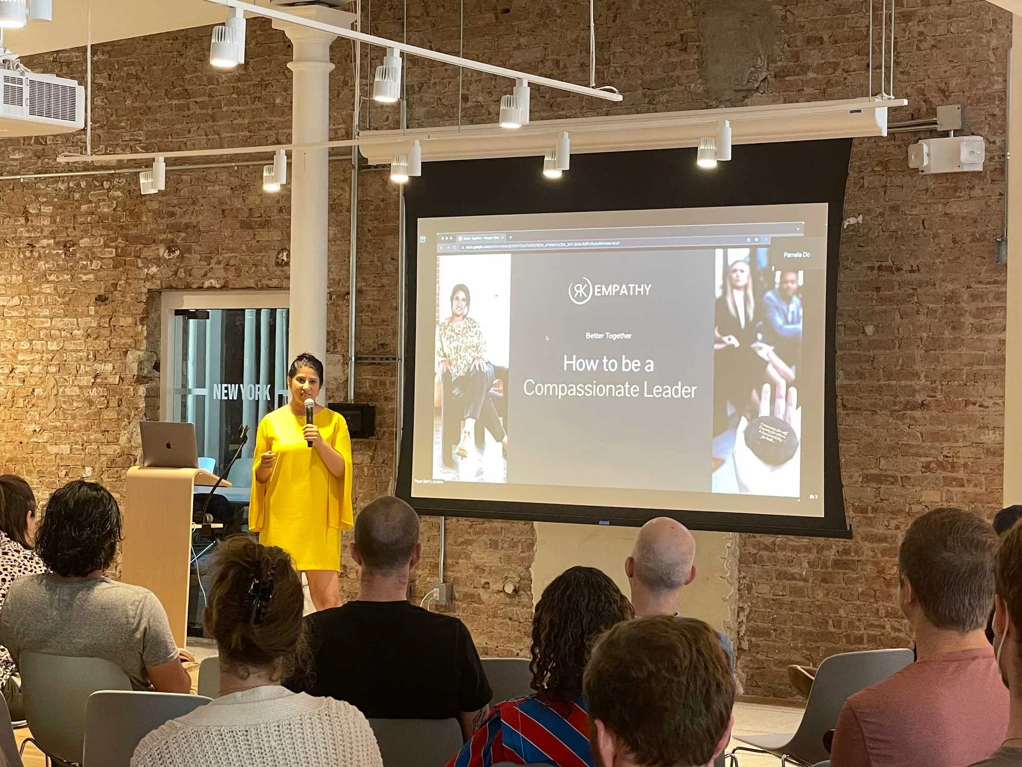 Dr. Payal Beri, PhD, speaking in front of a crowd with a projection of a slide deck that says "how to be a compassionate leader"