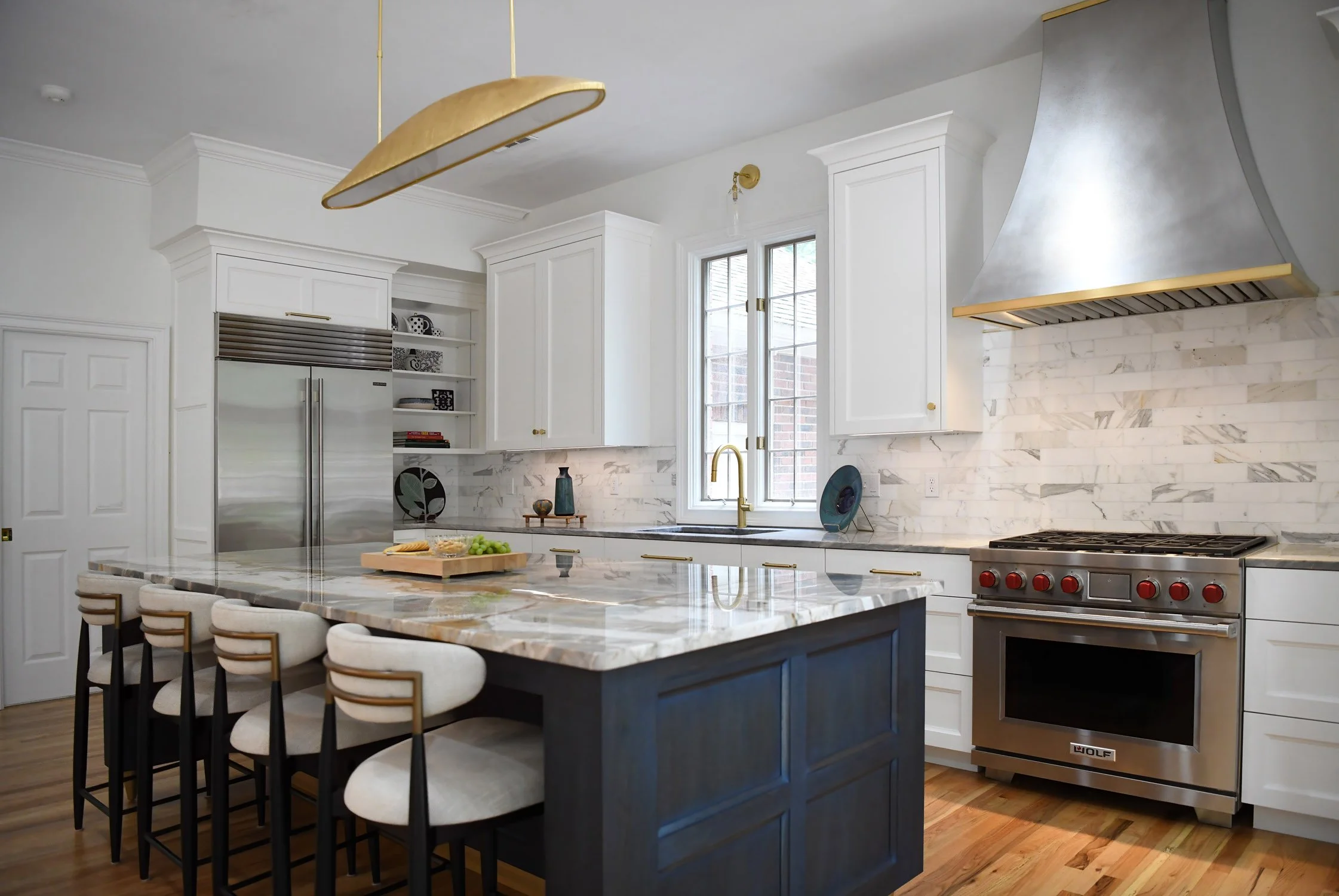 This transitional white kitchen features a custom stainless steel hood, Wolf range and Sub-Zero refrigerator. The large indigo stained walnut island with brass feet and quartzite top is a showpiece.
