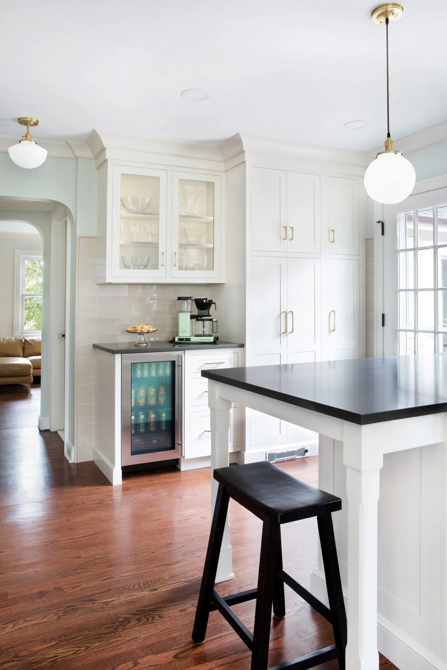 This bright transitional kitchen with off-white and muted pastels and dark countertops has the perfect layout with large peninsula and seating. There are vintage brass accents in hardware and lighting.