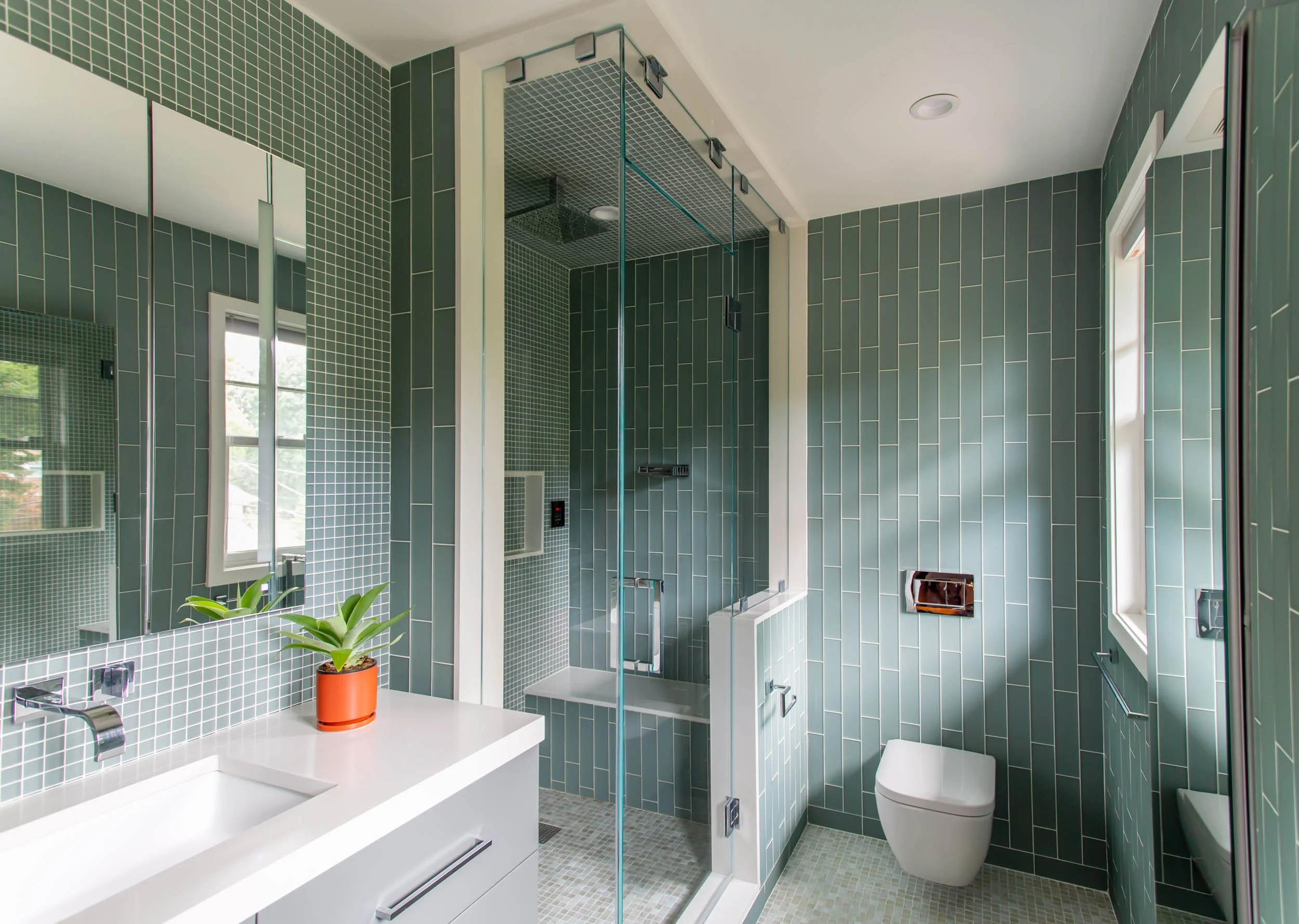 A European hotel inspired modern primary bath has spa-like features geared for relaxation. The turquoise green glass tiled surrounds the Dornbracht steam shower and features a waterfall module over the bench.