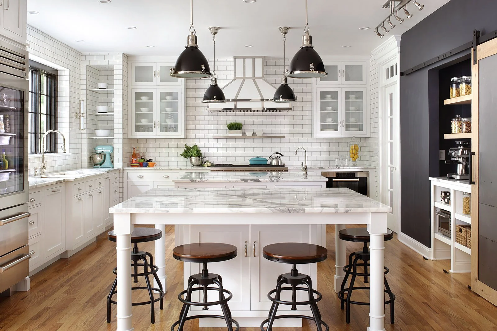 This white kitchen with industrial twist using metal accents on custom hood, pendants, barn door and Galley Sink. Statuary marble countertops and Wolf & Sub-Zero appliances make this a classic kitchen.