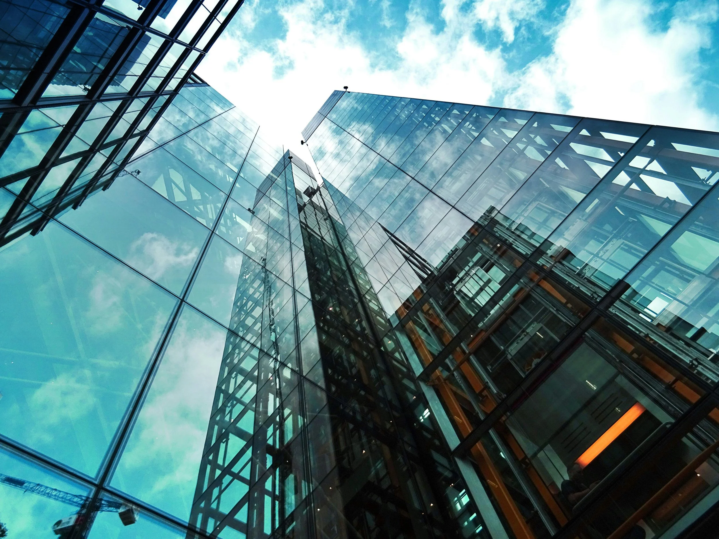 View from below of modern glass skyscrapers with reflections of the sky and clouds.