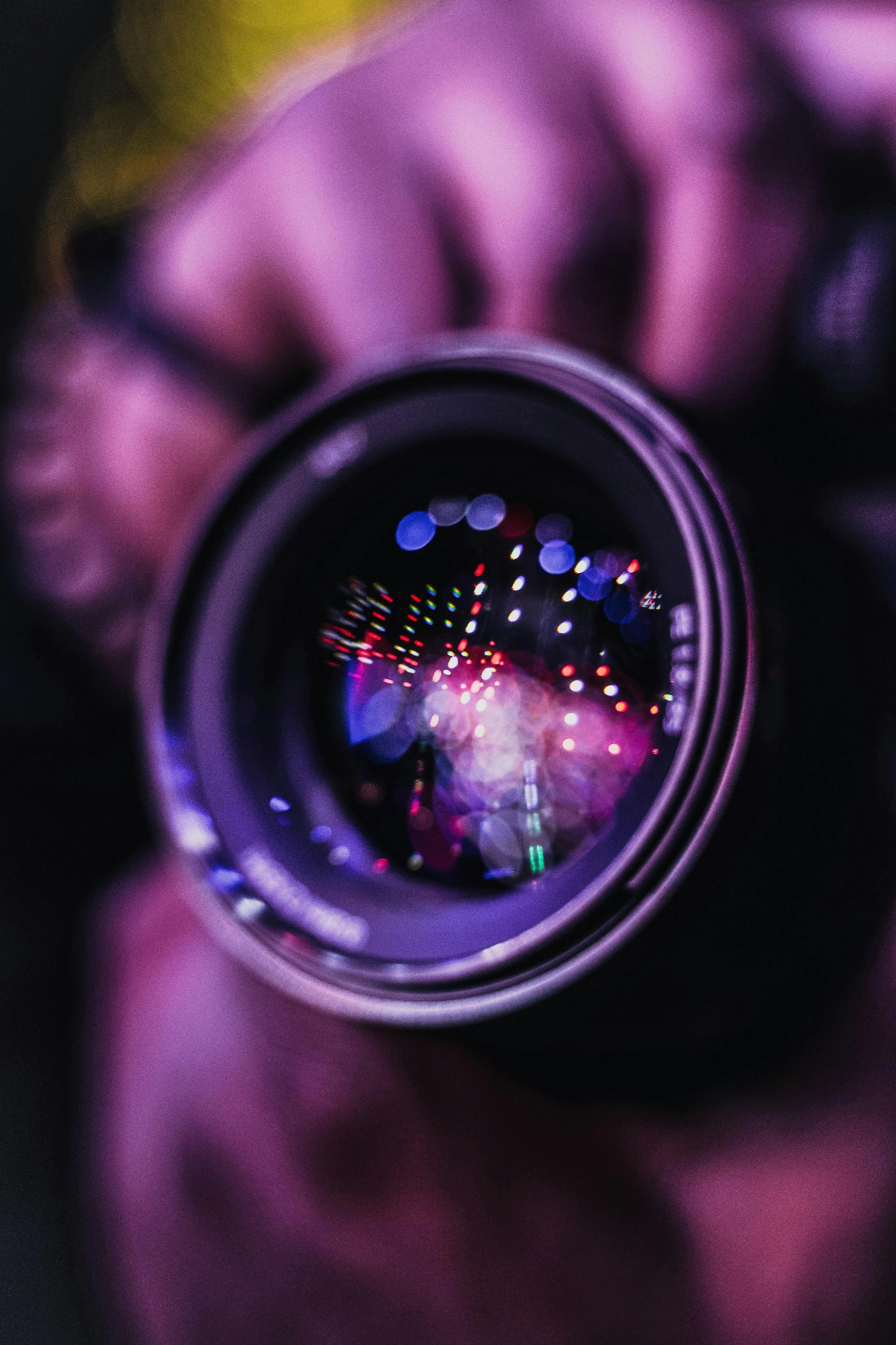 Close-up of a camera lens reflecting colorful lights, held by a person with a blurred background.