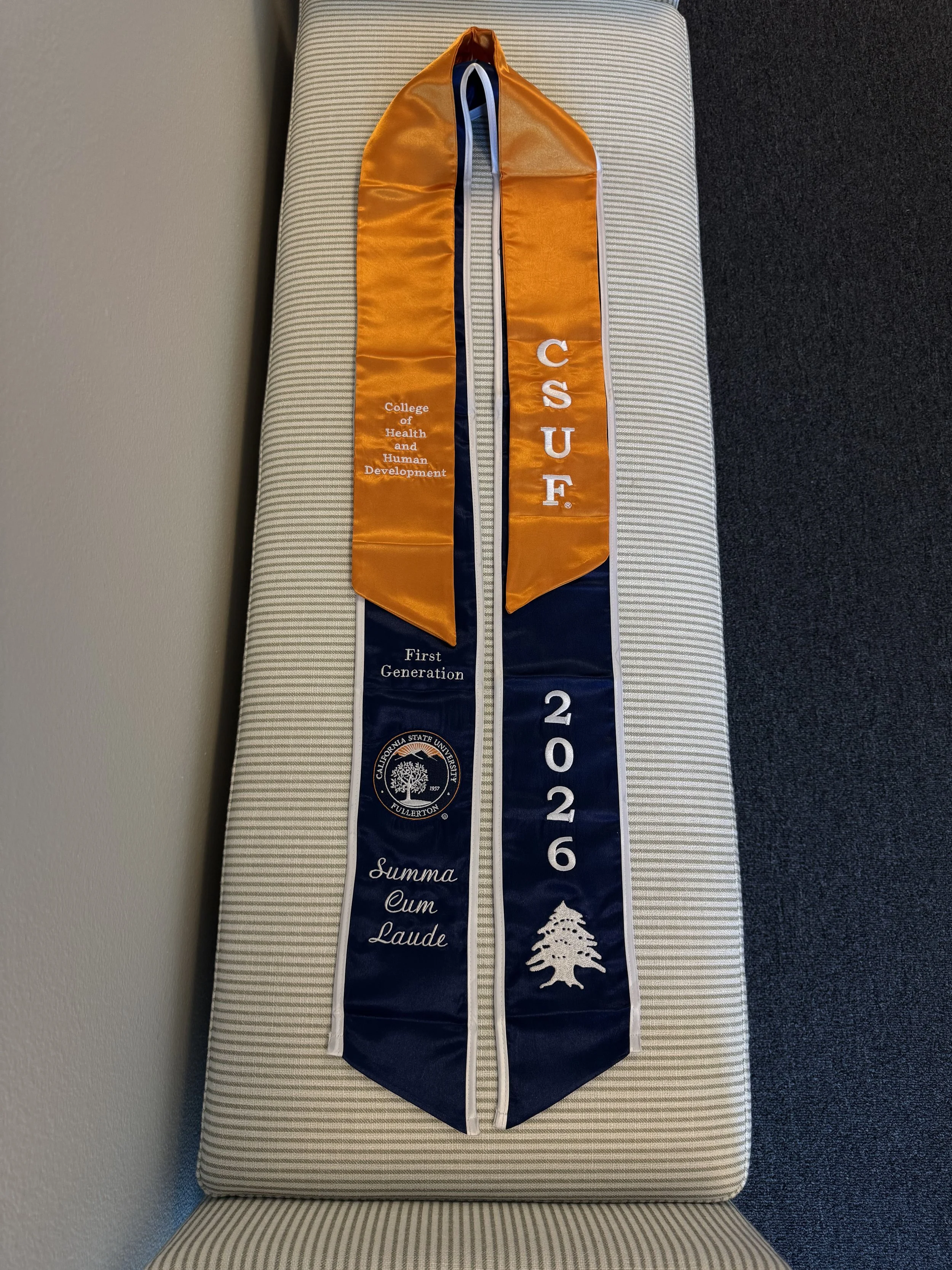 Colorful academic stole with orange, navy blue, and white sections, embroidered with 'College of Health and Human Development,' 'CSUF,' and a white tree crest. Embroidered Sash.