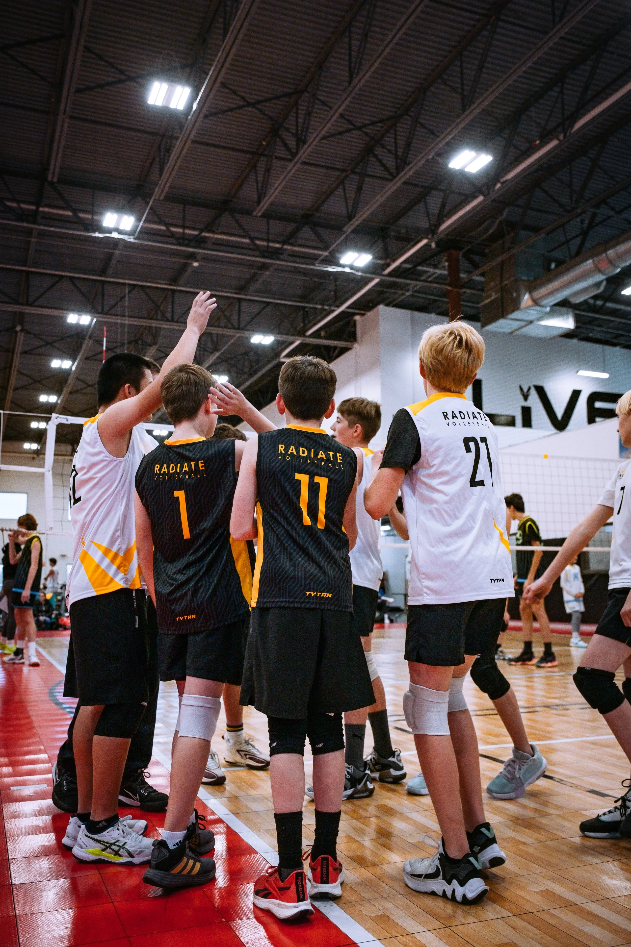 Youth volleyball team in huddle during game in indoor gymnasium.