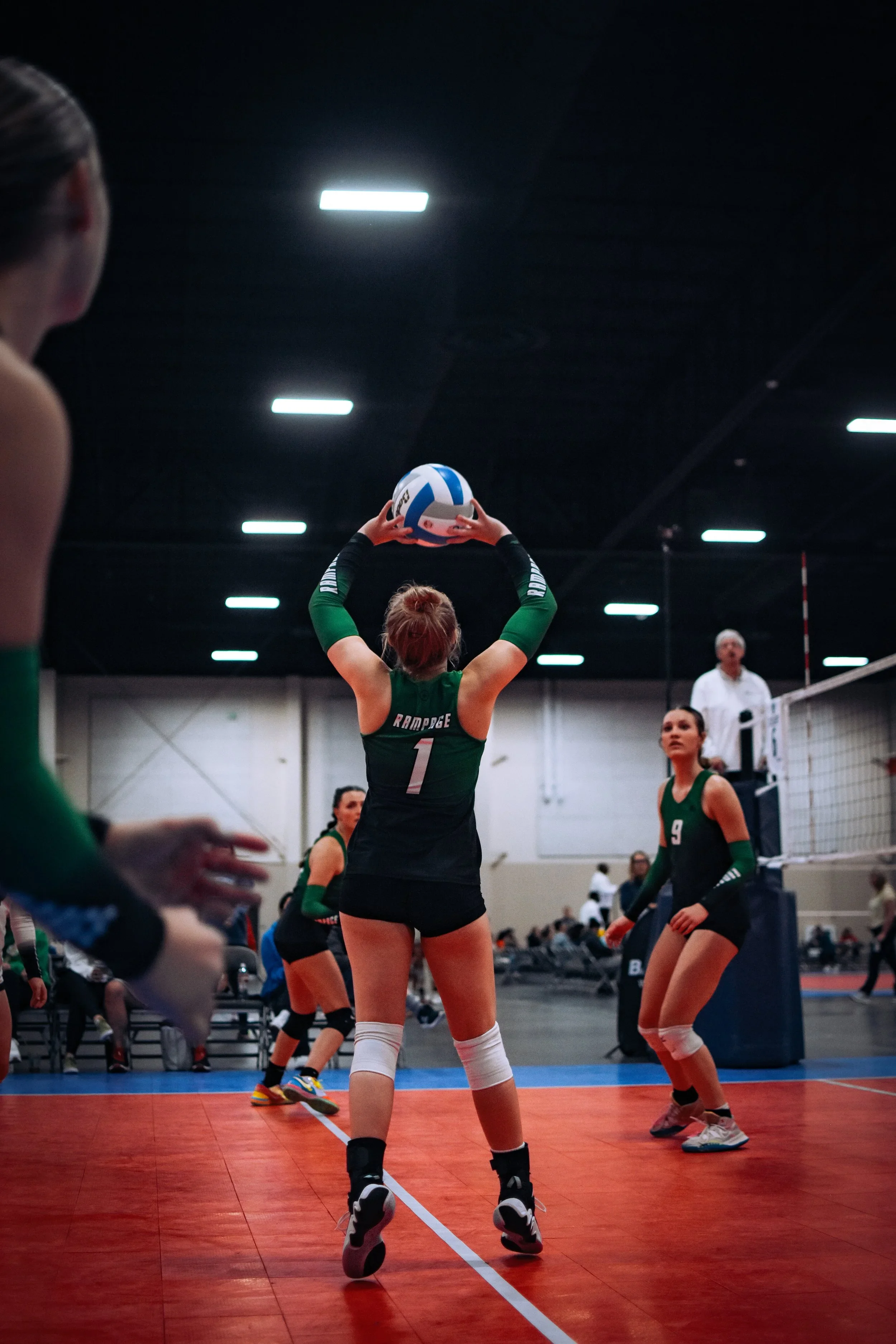 A volleyball player with jersey number 1 preparing to set the ball during a match in an indoor gym.