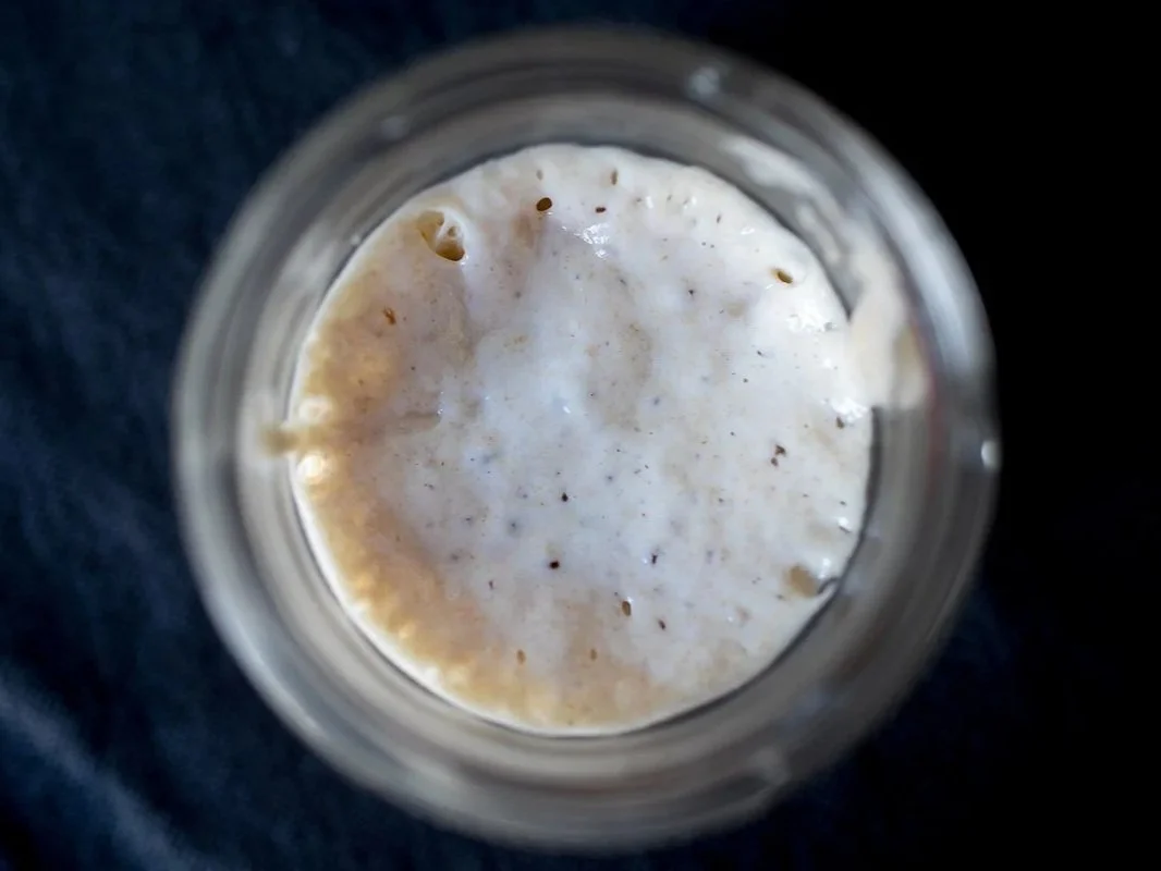 Close-up view from above of a frothy, sourdough starter in a glass jar, with visible bubbles ready for use.