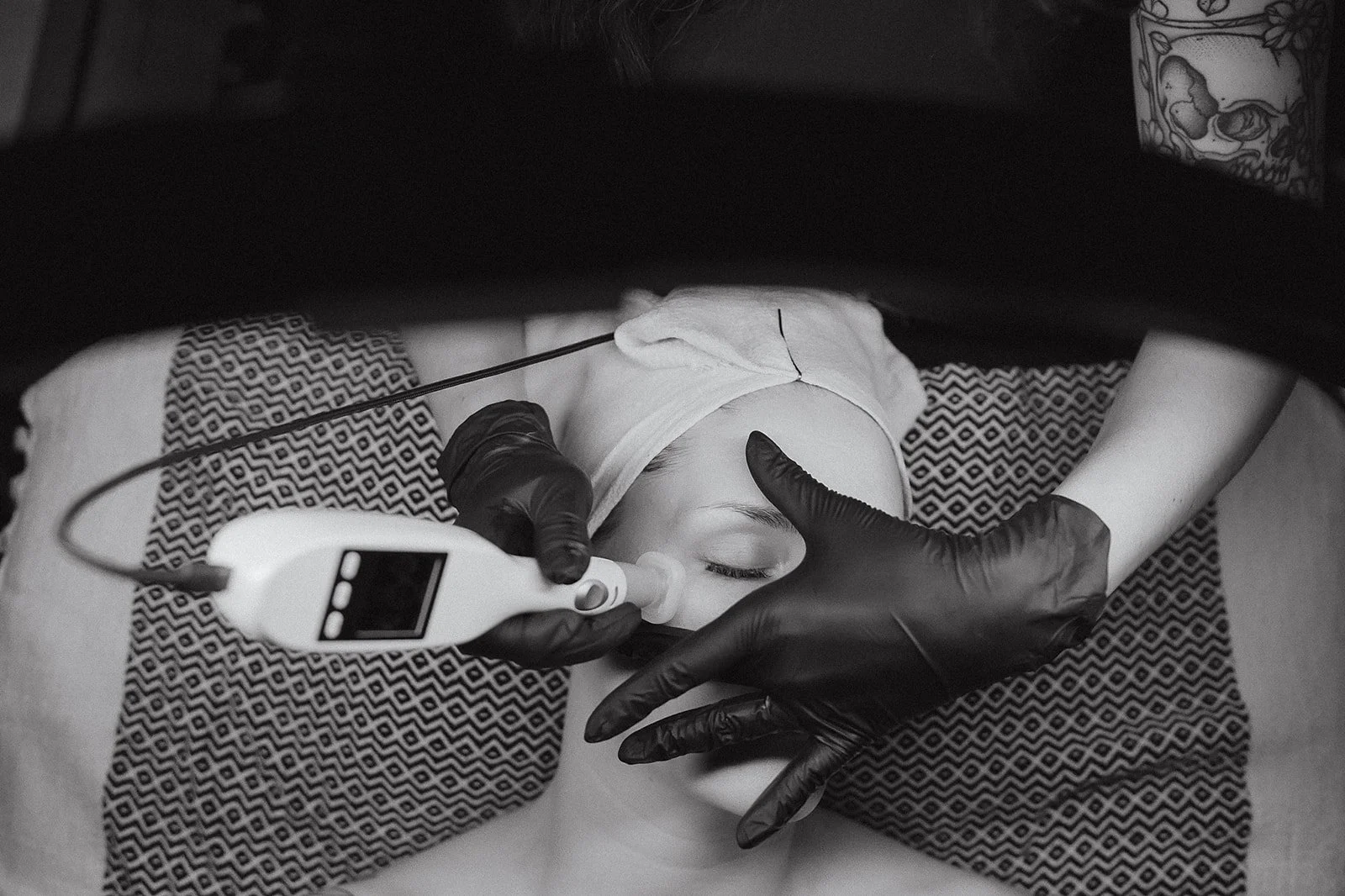Amanda Jerman licensed esthetician and owner of Healing Vibes Esthetics Denver with black gloves administering a Jet Plasma skincare procedure with a handheld device on a woman's face lying on a pillow.