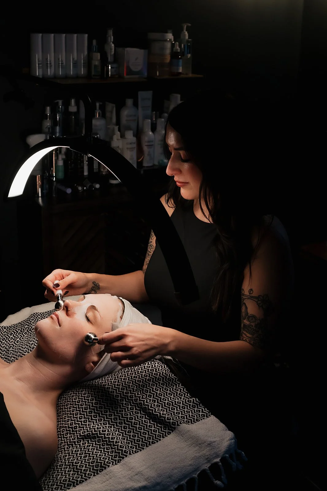 A woman lying on a treatment bed with her eyes closed, receiving a facial treatment with small metal tools from Amanda Jerman licensed esthetician in the Healing Vibes Esthetics Denver skincare clinic.
