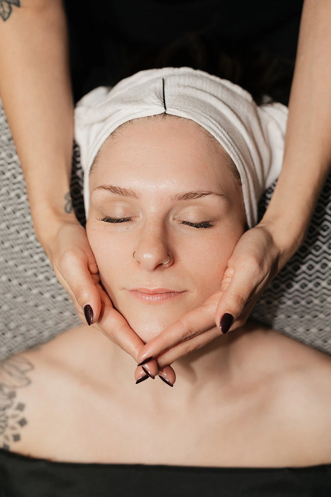 A woman receiving a relaxing facial massage while lying down with her eyes closed.