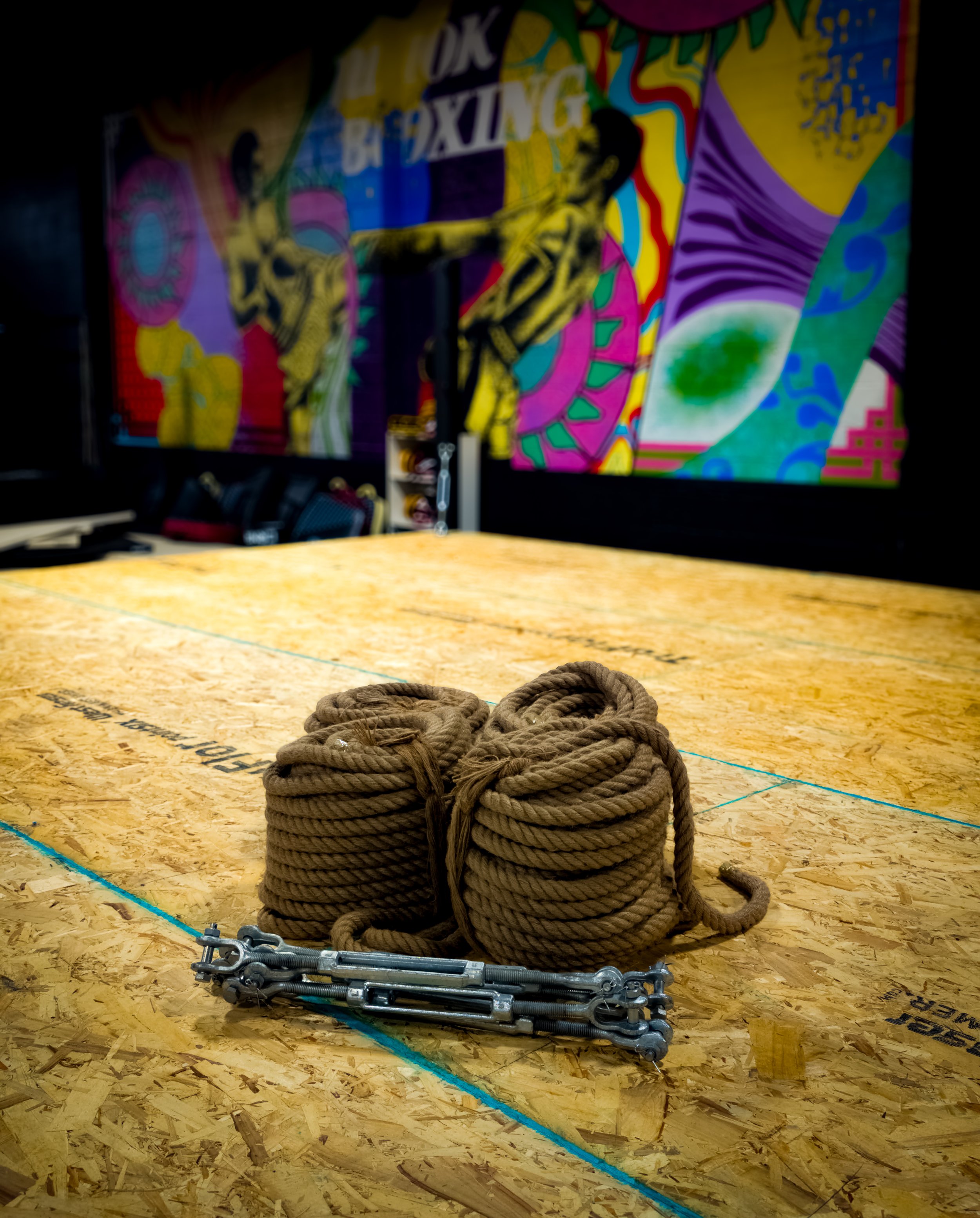 Rope and turn buckles sitting on top of the wood base of a new custom boxing ring. 